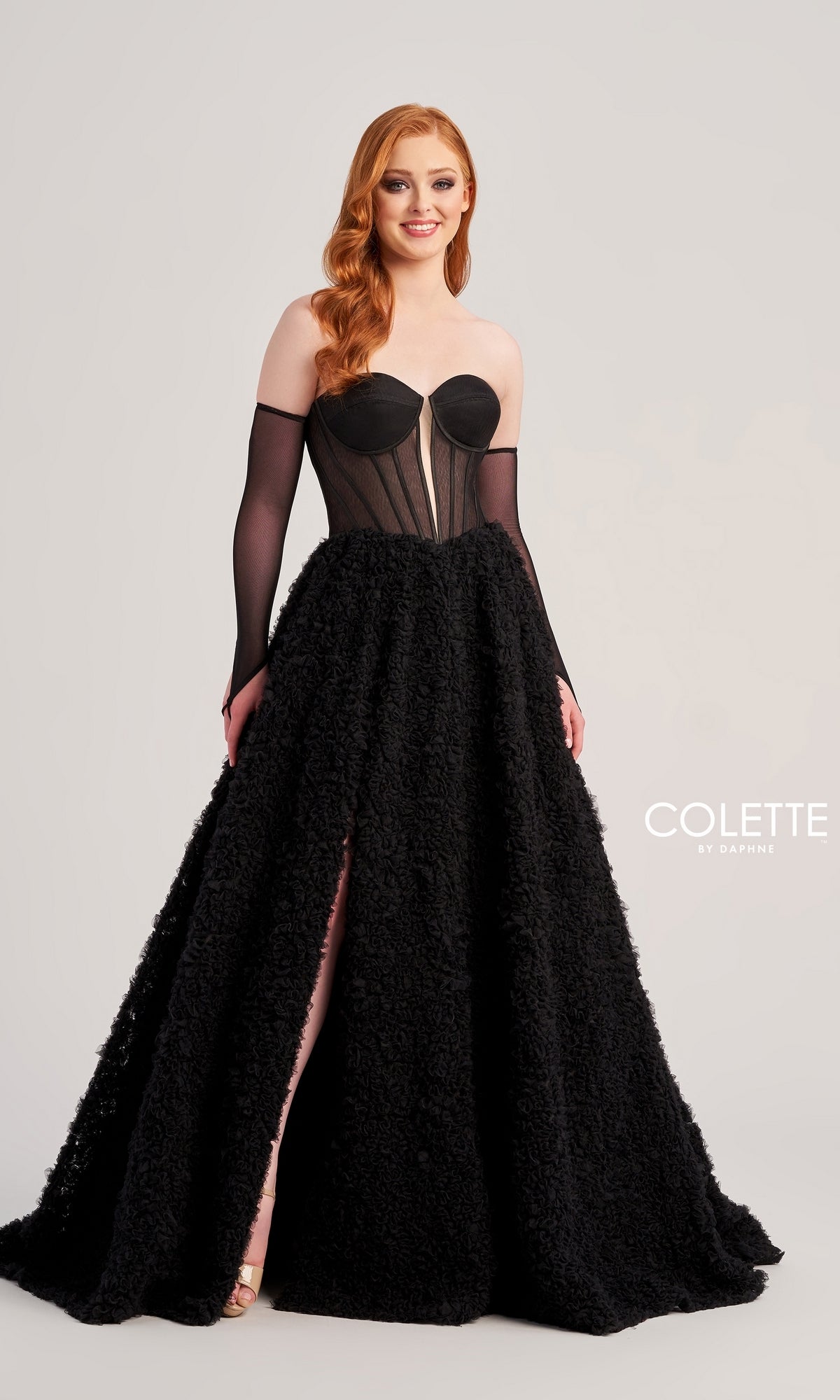A woman with long red hair wears the Bustier Colette Long A-Line Prom Ball Gown CL5114, featuring a sheer corset bodice, strapless neckline, textured full skirt, and long black gloves. The Colette by Daphne logo appears in the corner.
