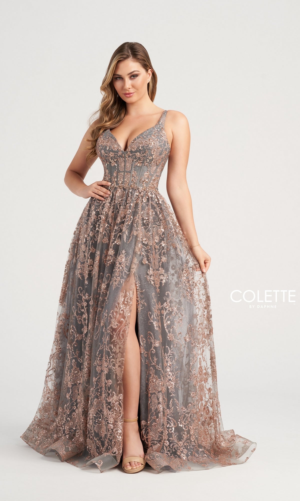 A woman models the Glitter-Tulle Colette Long Prom Dress CL5134, a sleeveless, floor-length gown with a corset-style bodice and front slit, embellished with lace, sequins, and delicate detailing against a light background.