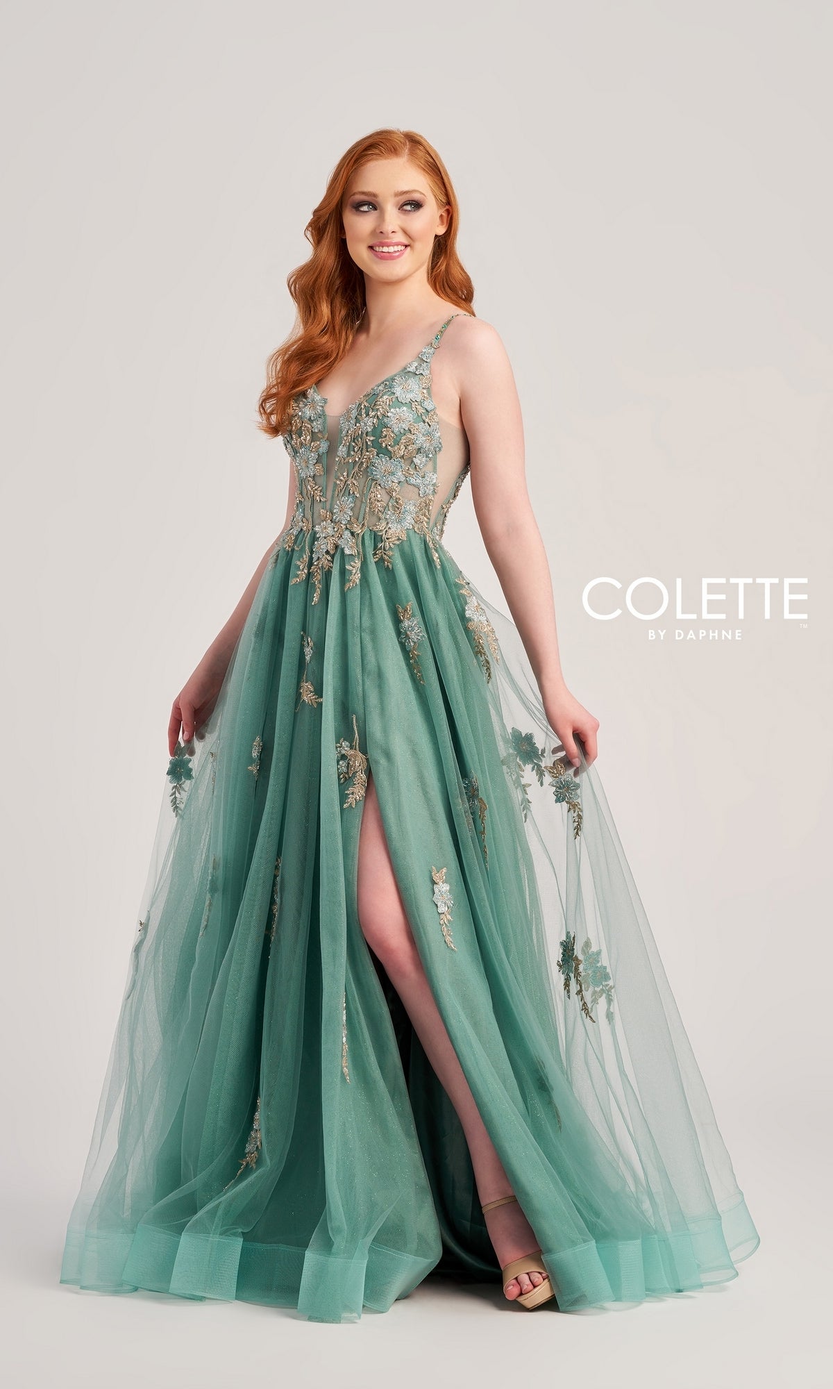 A woman in a sleeveless teal Glitter-Lace Colette Designer Prom Gown CL5143 with corset-back poses against a plain background. The ball gown features floral embroidery, a thigh-high slit, and elegant lace details.