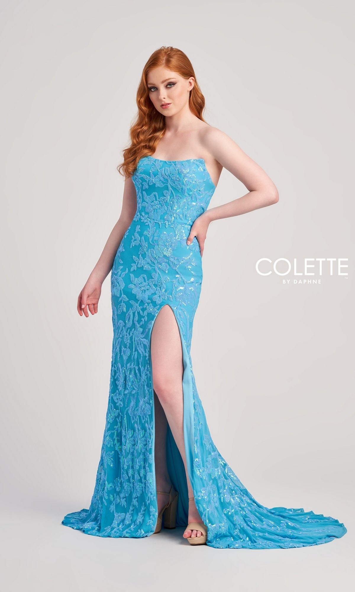 A woman with long red hair wears the Colette Strapless Sequin Long Prom Dress CL5238, featuring a corset-style bodice, curve-hugging skirt with floral patterns, and a thigh-high slit.