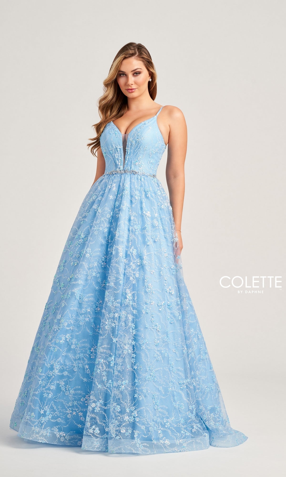 A woman models the Glitter-Tulle Colette Long Prom Ball Gown CL5288—light blue, floor-length, with lace details, a beaded waist, and a deep V-neck—standing before a plain background with