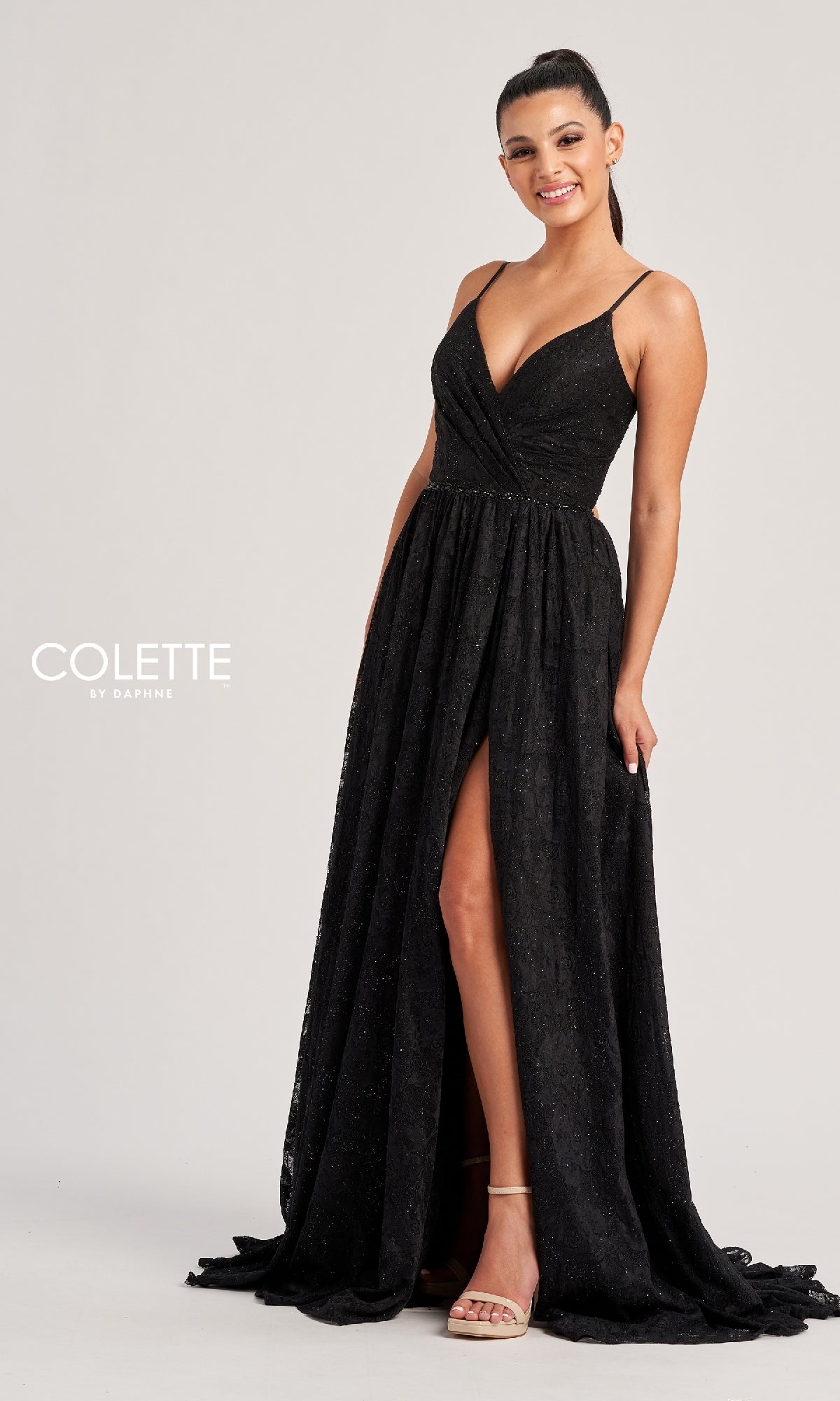 A woman in the Colette CL8010, a sleeveless floor-length black glitter prom dress with spaghetti straps and a front slit, stands smiling against a plain background.