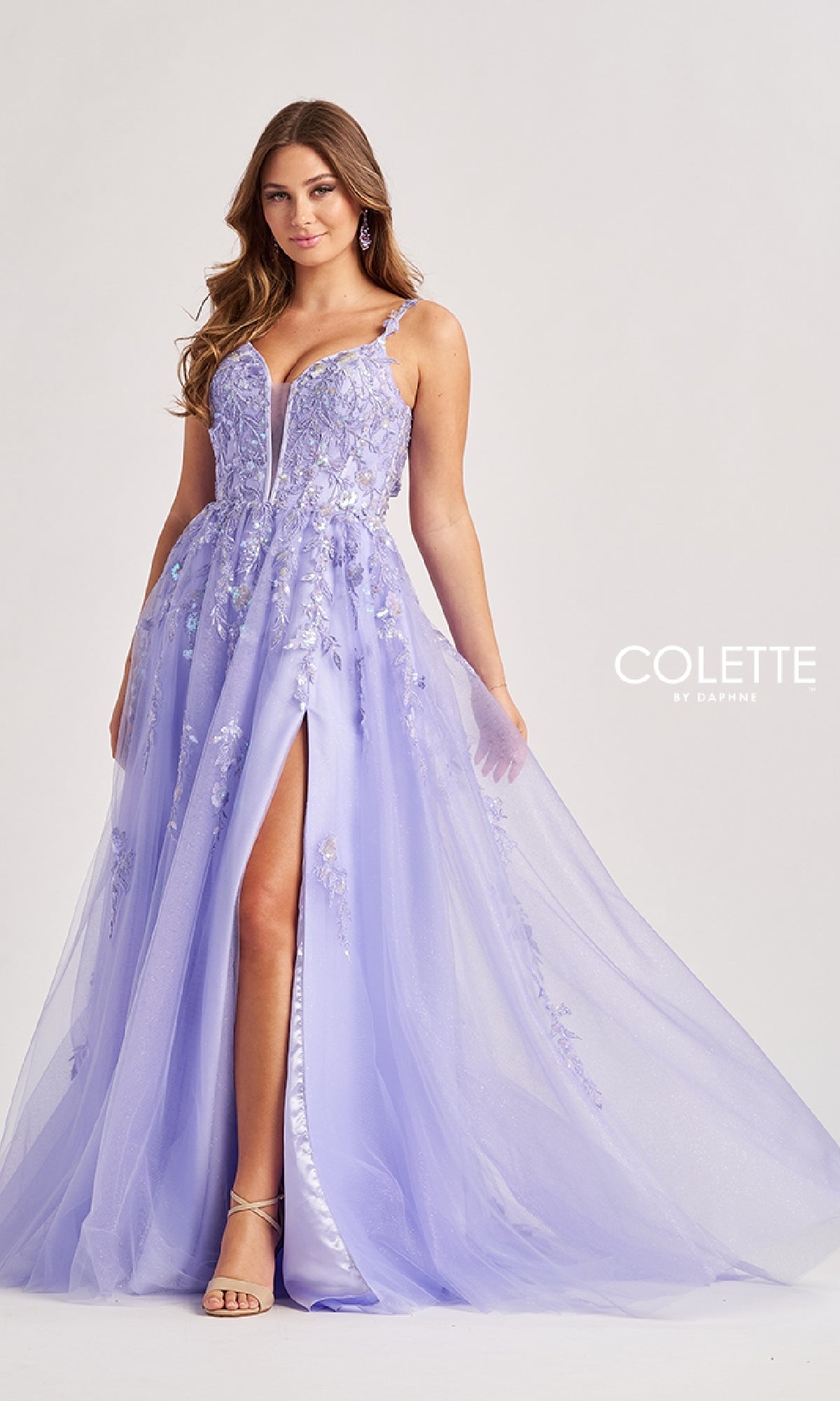 A woman models the Colette CL8060, a long light purple prom dress with floral embellishments, spaghetti straps, deep V-neckline, high front slit, and elegant embroidery against a plain background.