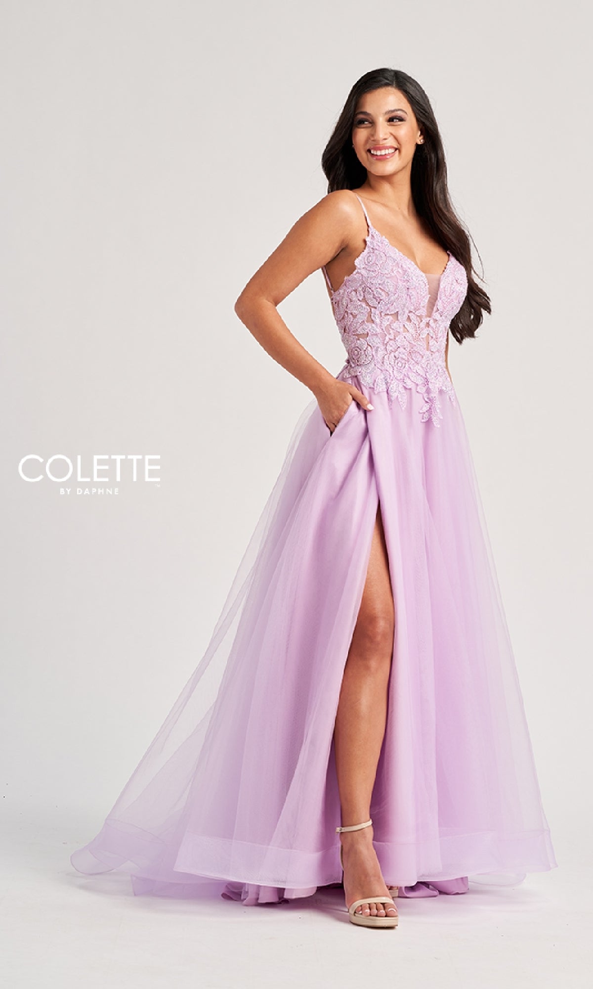 A woman smiles in the Long Prom Dress: Colette CL8100, featuring a pastel hue, lace-embroidered bodice, thin straps, tulle skirt, and thigh-high slit. The