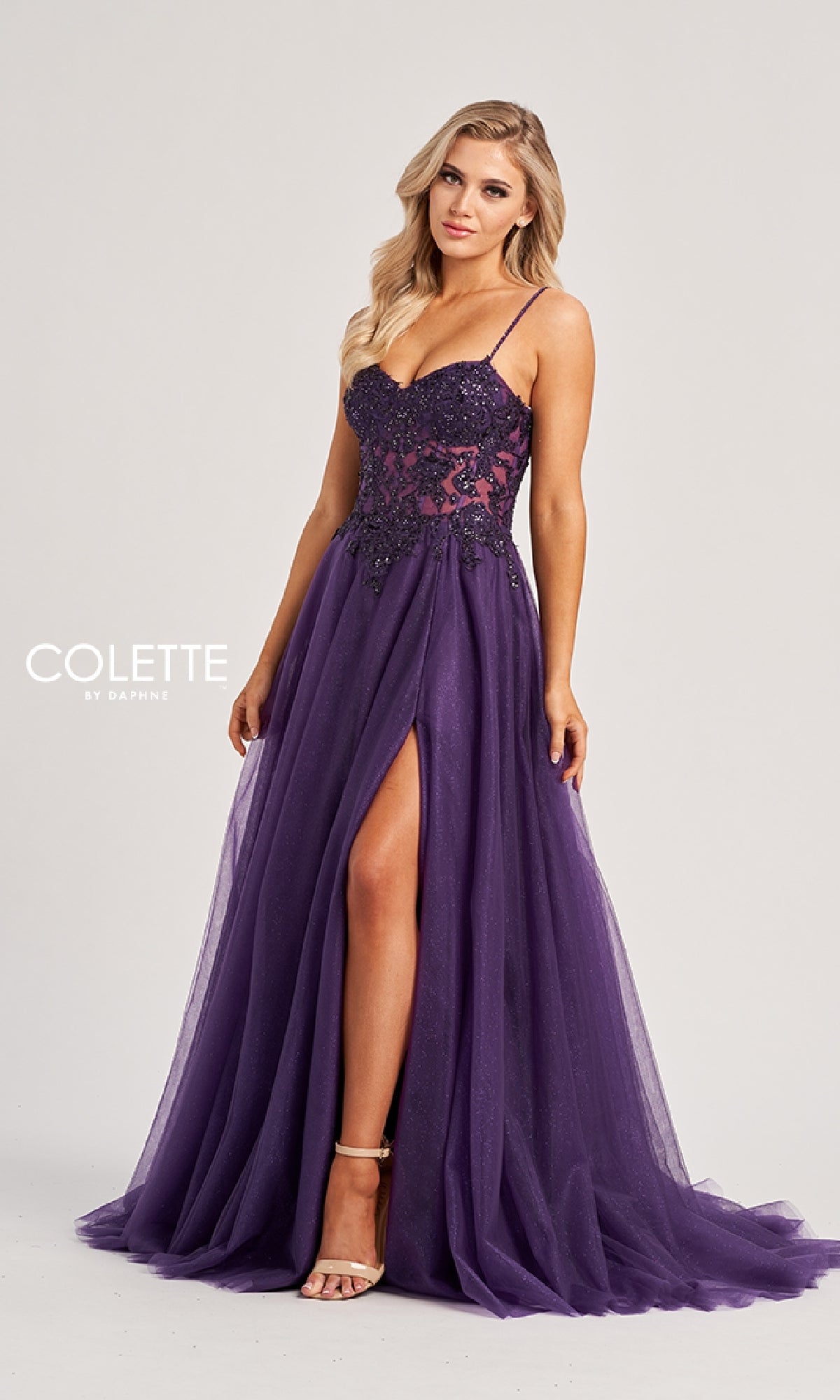 A woman wears the Colette CL8280, a sleeveless, floor-length purple sequin prom dress featuring a sheer bodice, beaded accents, and a high front slit, standing against a plain background.