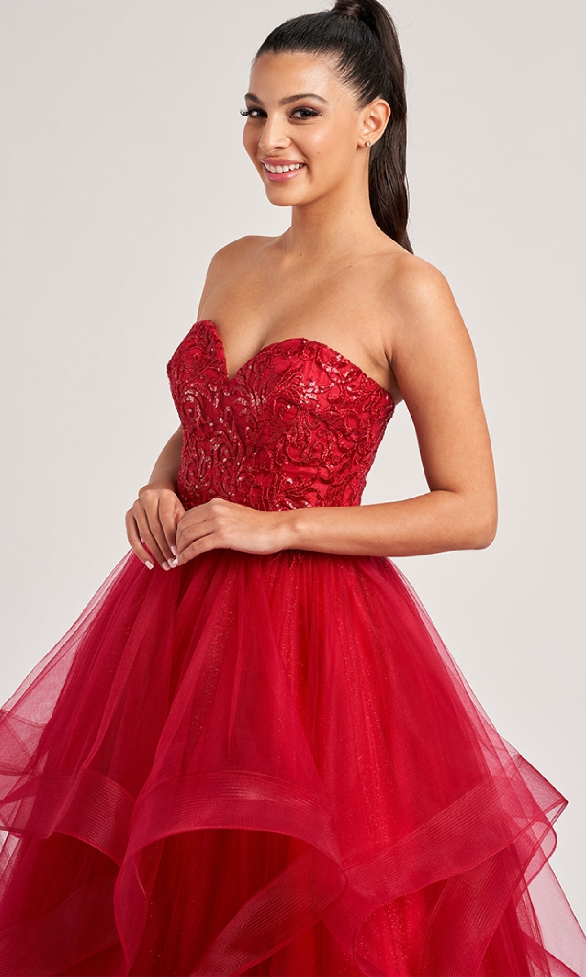 Woman wearing the Colette CL8290 long prom dress with a strapless, embroidered sequined bodice and layered tulle skirt, smiling against a plain background.