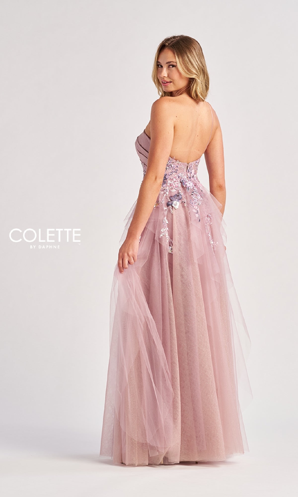A woman models the Colette CL8400 Long Prom Dress—a light pink, strapless, floor-length gown with floral sequin details and a flowing tulle A-line skirt—posing slightly turned from the camera.