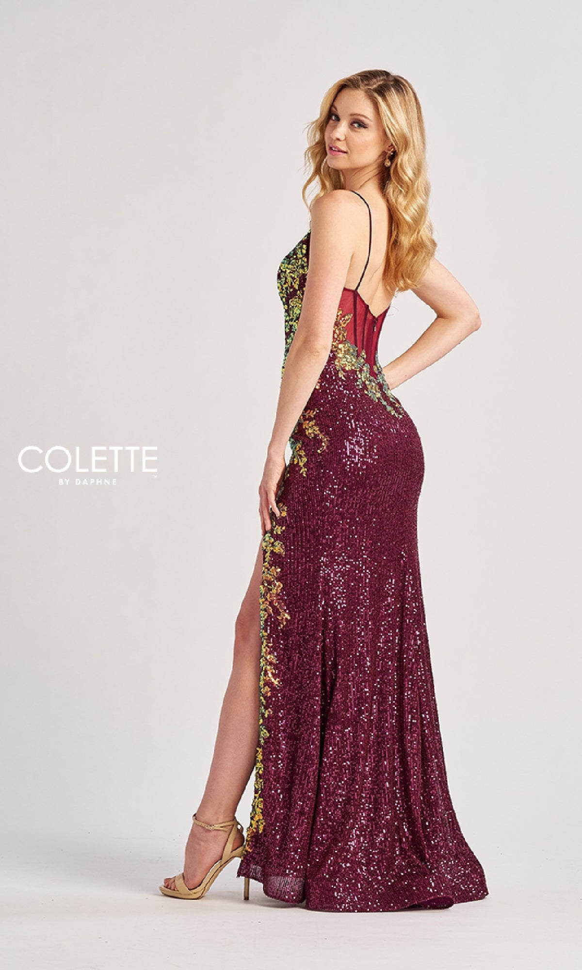 A woman stands sideways, looking over her shoulder in the Long Prom Dress: Colette CL8425—a sleeveless, floor-length sequin gown with gold detailing and a corset bodice—set against a plain backdrop.