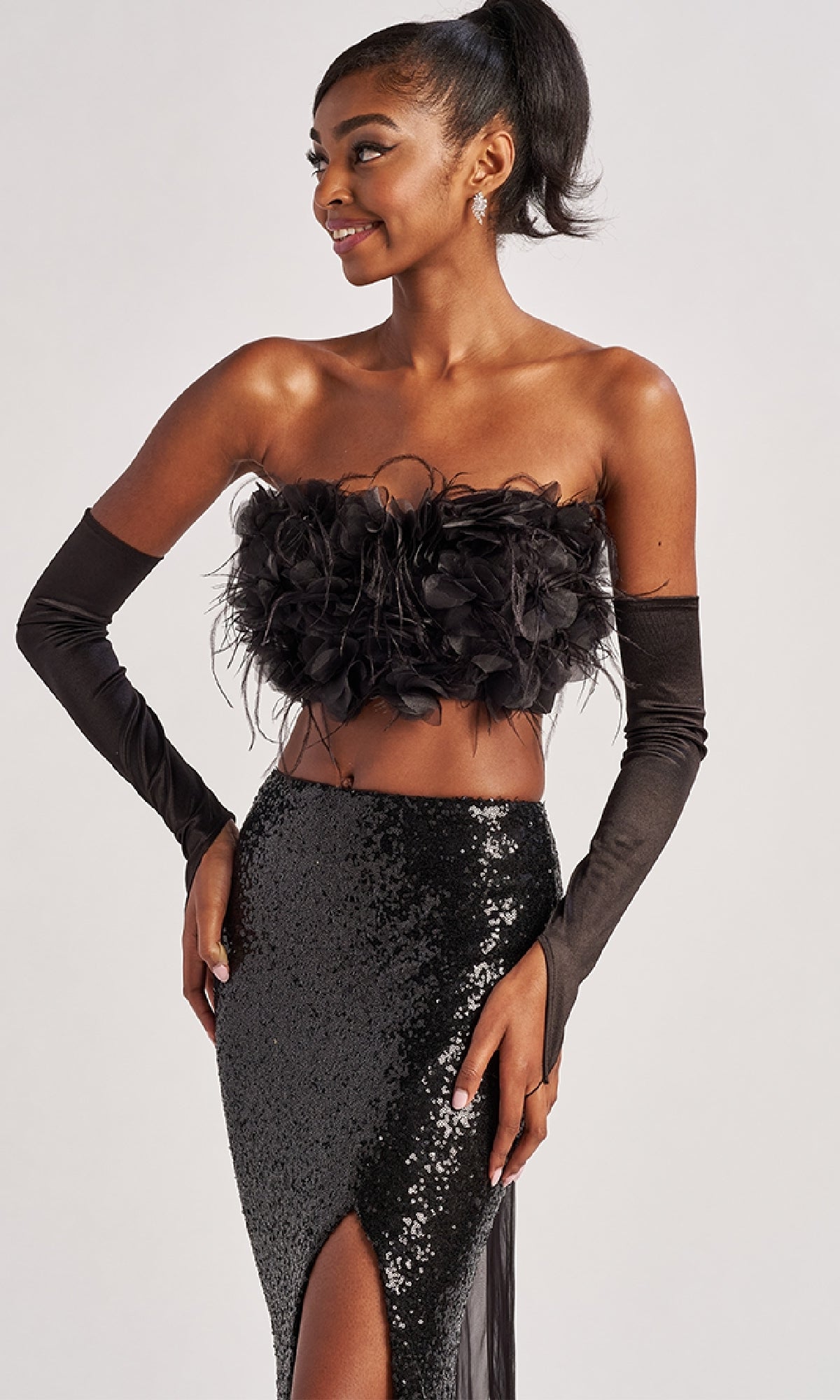 Woman wearing the Colette CL8450 Long Prom Dress—a sequined, floor-length gown with a thigh-high slit—standing and smiling against a plain background.