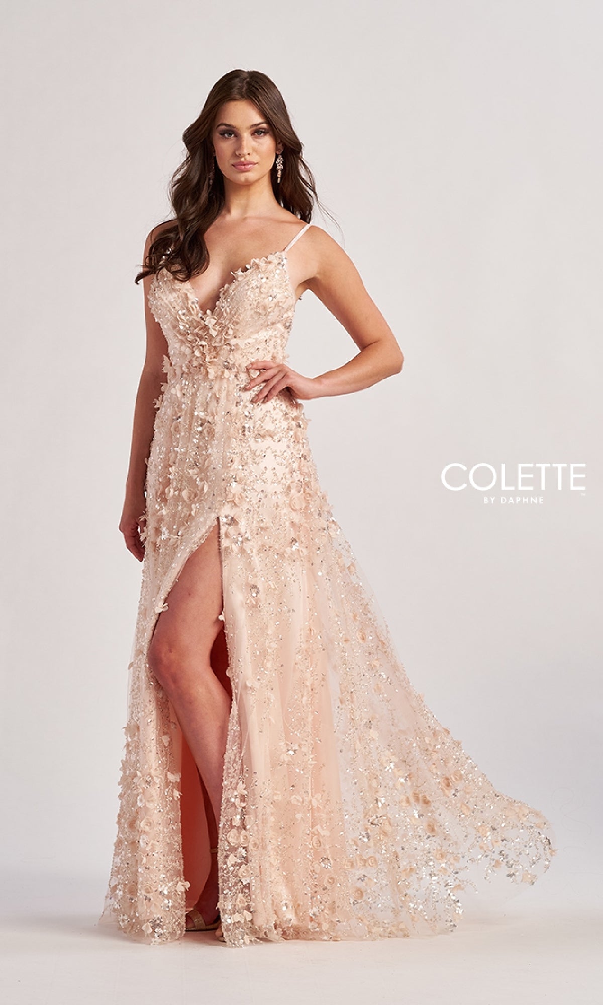 A woman models the blush pink, sleeveless Colette CL8525 long prom dress with a high slit, floral embellishments, and a deep V-neckline against a plain background.