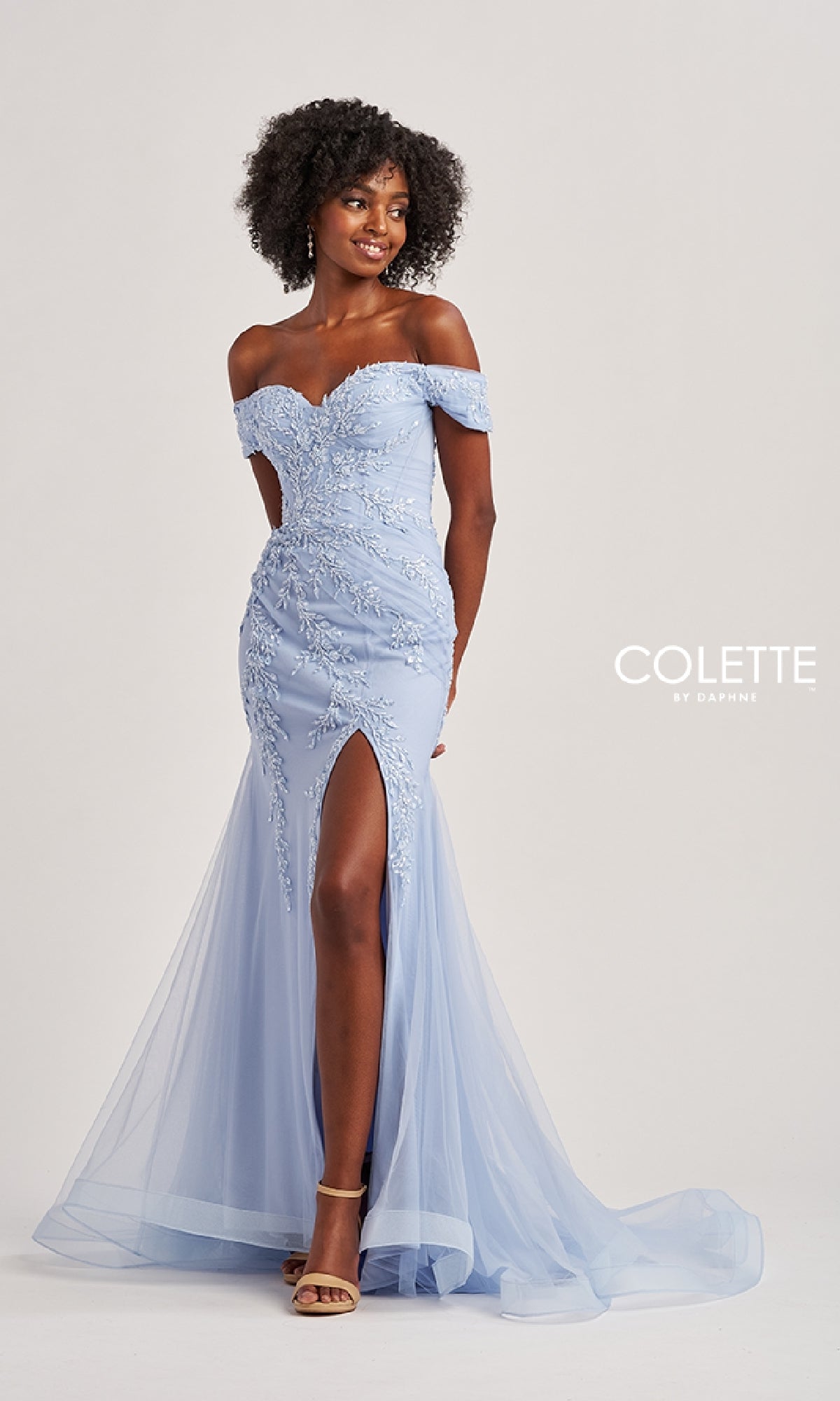 A woman models the Colette CL8645 Off-the-Shoulder Long Prom Dress in light blue, featuring beaded floral embroidery, a thigh-high slit, mermaid silhouette, and tulle overlay against a plain background.