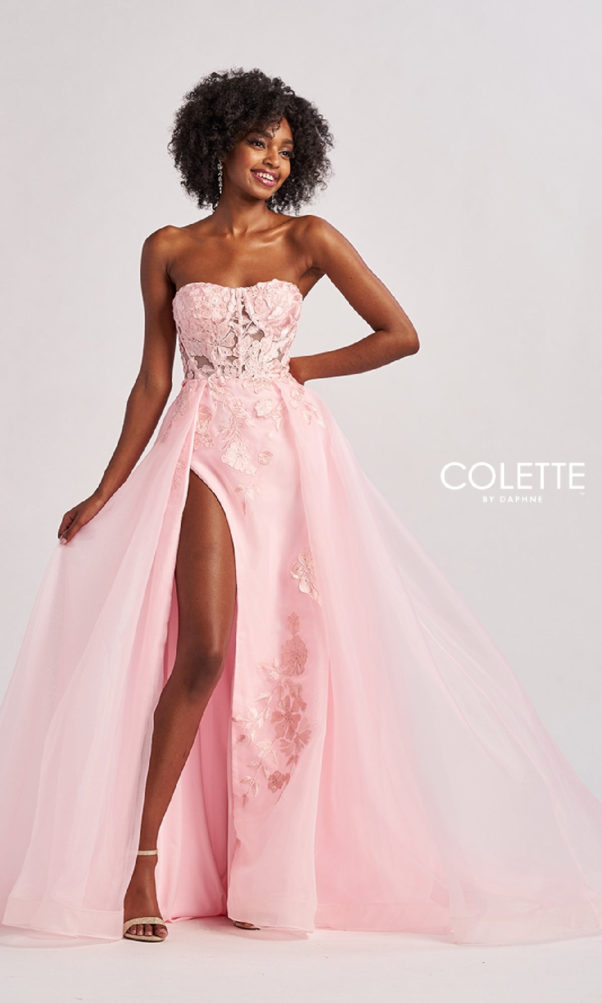 Woman wearing the Colette CL8660 long prom dress with a strapless sheer lace bodice and embroidered floral A-line skirt, standing against a plain white background.