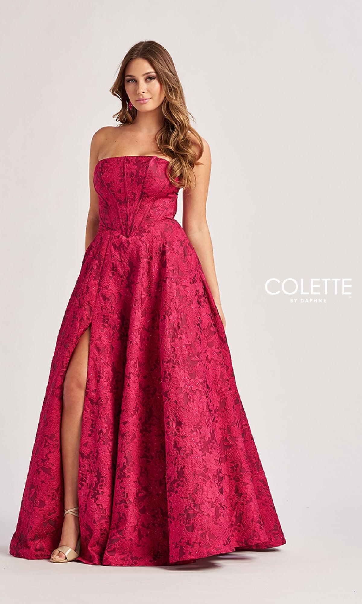 A woman models the Colette CL8675 long prom dress—strapless, floor-length red lace featuring an a-line skirt and front slit—standing against a plain background with