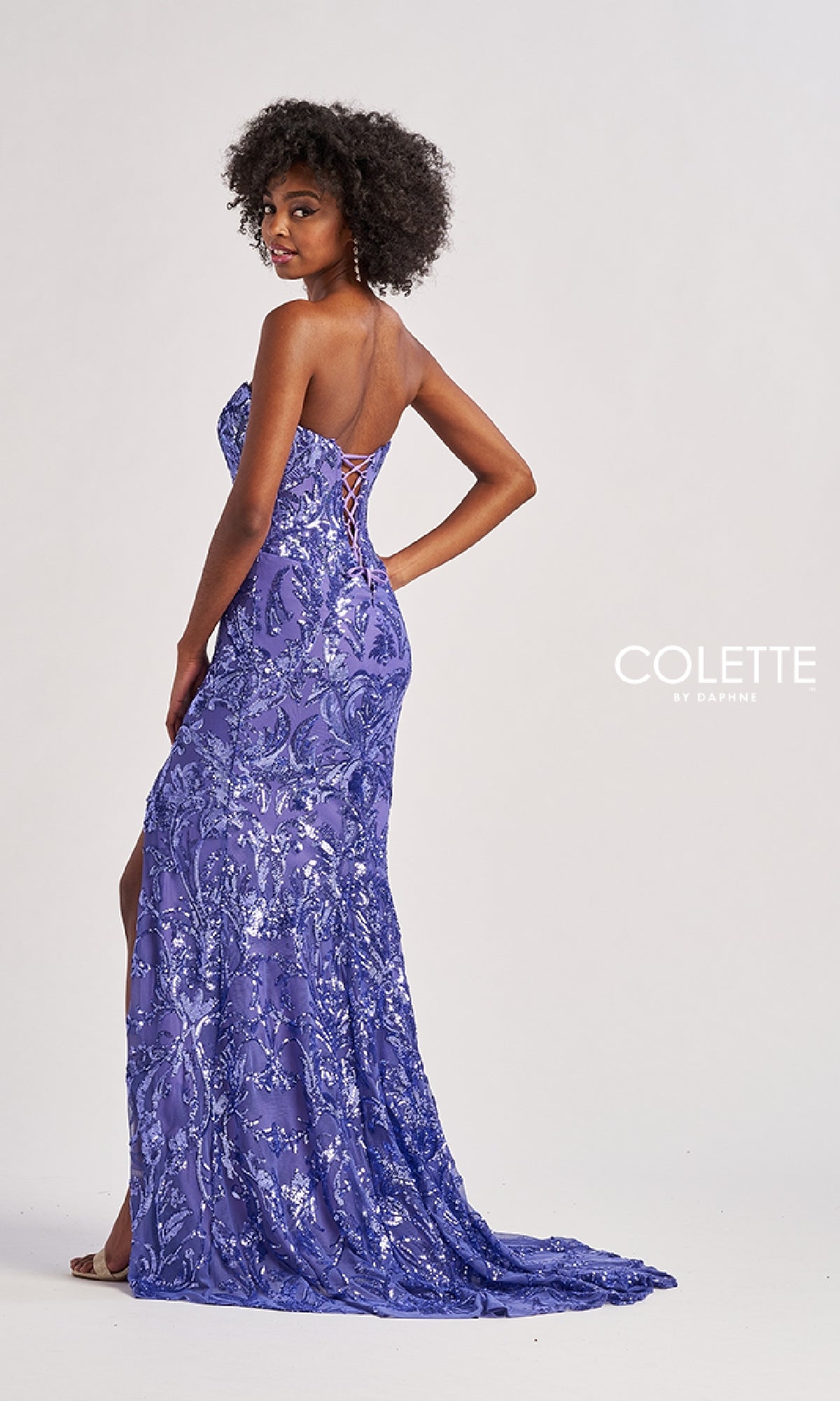 Woman in the Colette CL8680 long prom dress, a strapless purple sequin gown with a lace-up back, standing sideways and glancing over her shoulder.