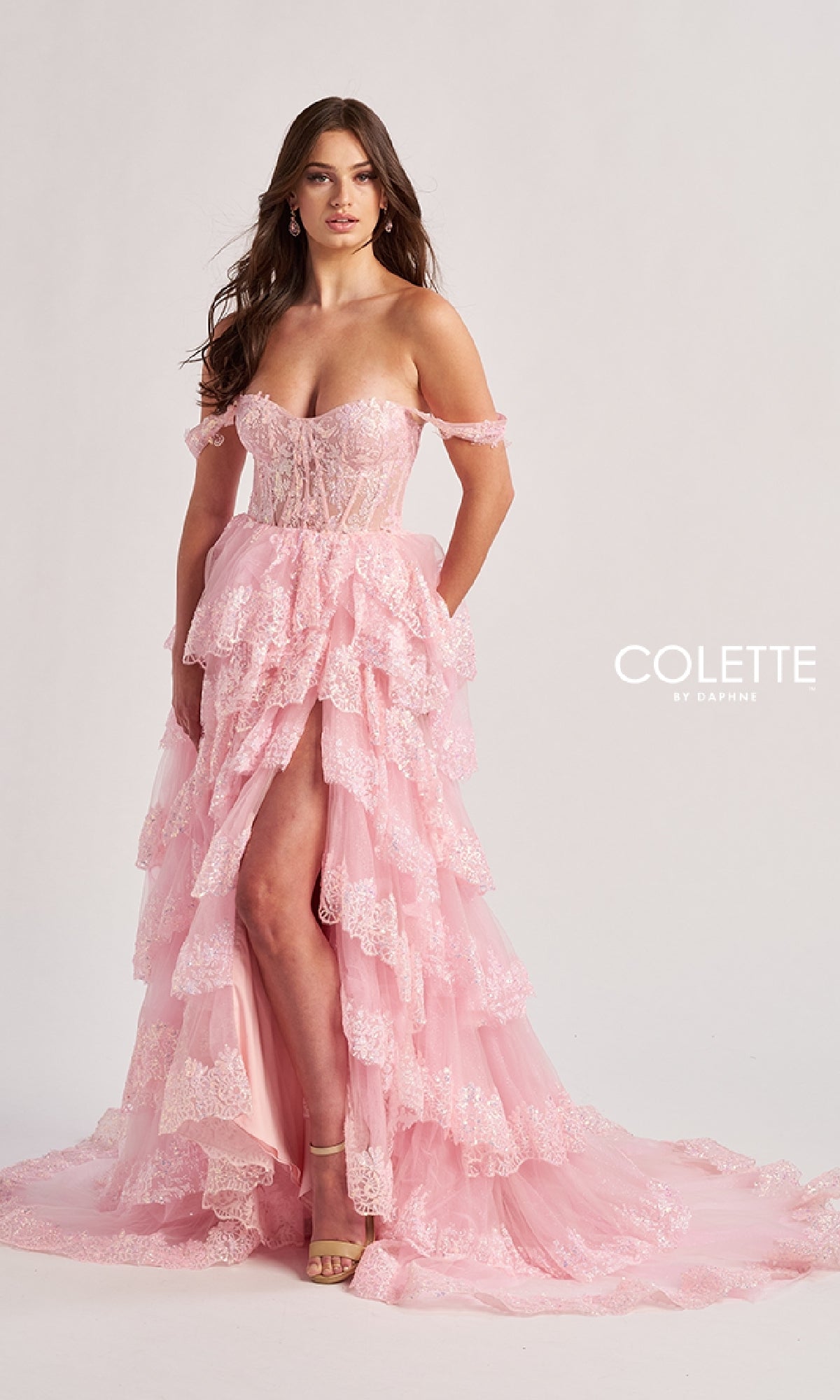 A woman models the Colette CL8690 long prom dress, featuring an off-shoulder pink lace bodice, ruffle tiered A-line skirt with high slit, against a plain light background.