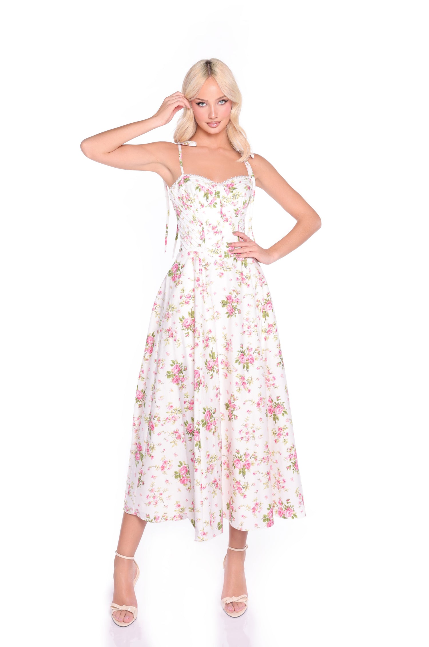 A woman models the Ivory Blush Floral Midi Casual Dress: Cecilia with a corset-style bodice and spaghetti straps, paired with open-toe heels, standing against a plain white background.