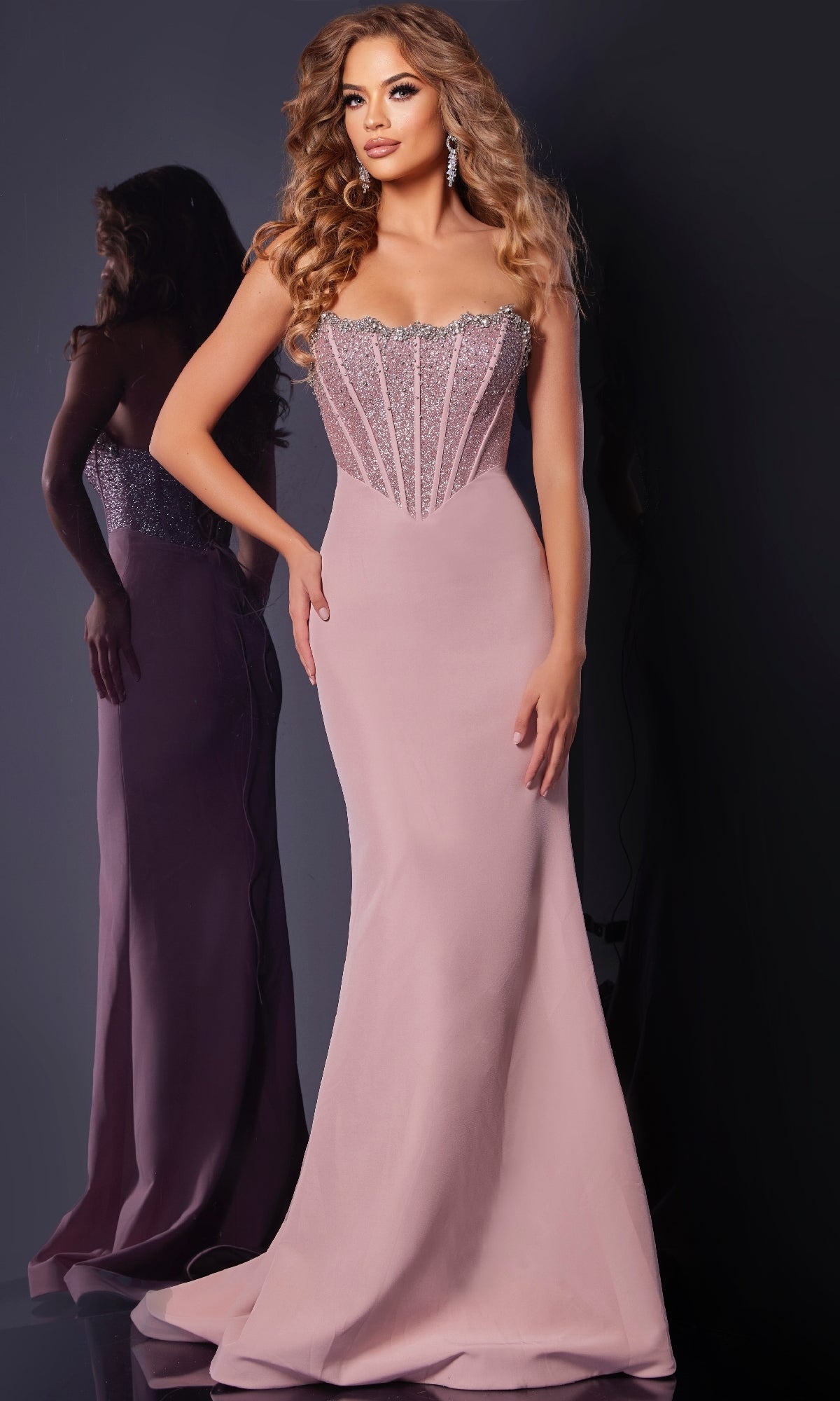 A woman in the Jovani D5310 long prom dress, featuring a fitted blush pink design with a sparkling beaded corset bodice, poses elegantly against a dark background.