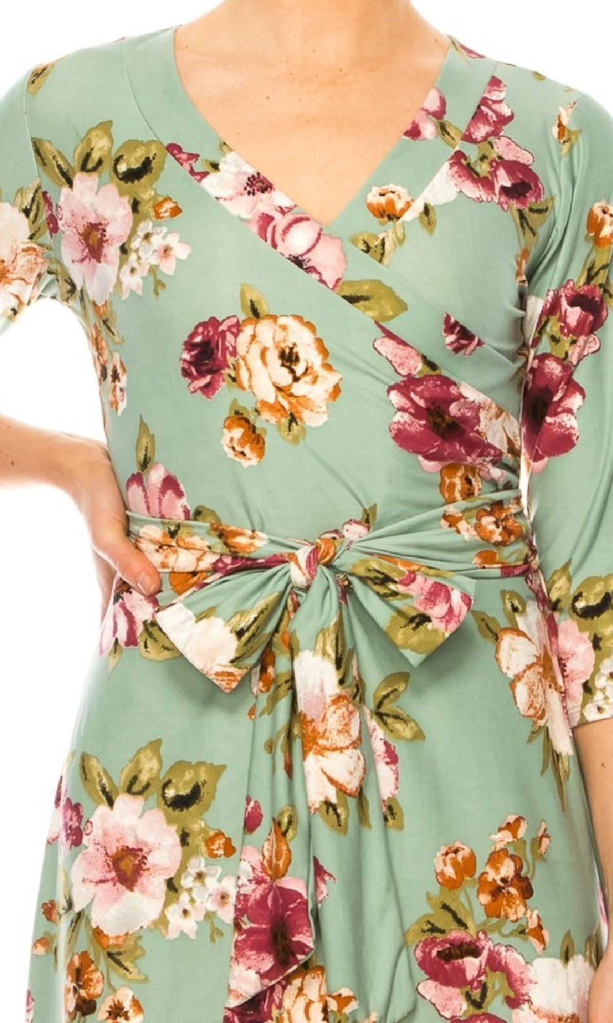 A person models the Sage Green Floral Print Faux-Wrap Casual Dress with a V-neckline, tied waist belt, and their left hand resting on their hip.