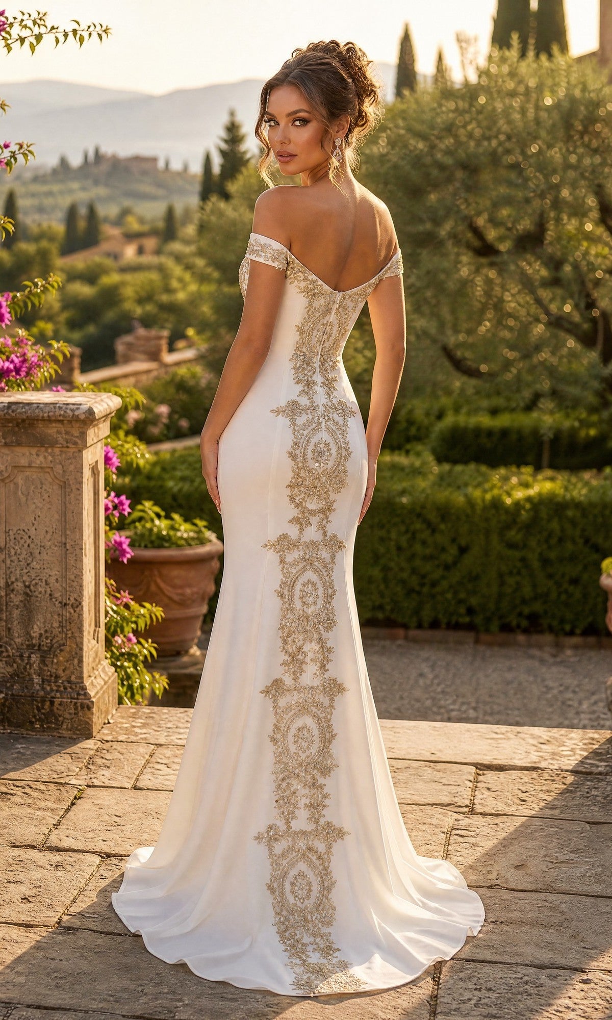 A woman wearing the Long Formal Dress: Chicas DM4011, featuring an elegantly off-the-shoulder design, intricately embroidered bodice, and delicate gold appliques, stands on a stone patio facing away, surrounded by lush greenery and distant hills.
