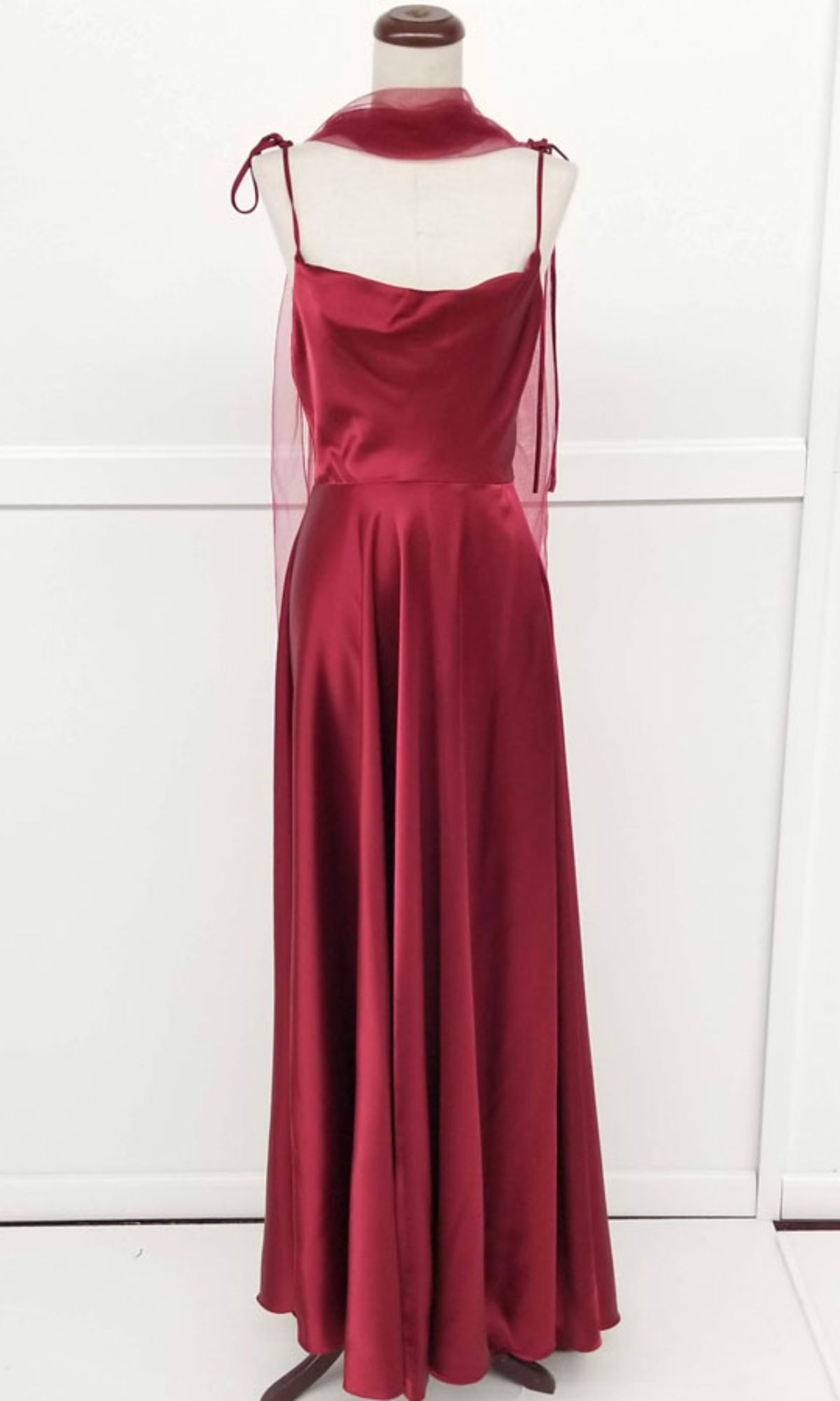 The Shoulder-Tie Long A-Line Prom Dress Chicas DM4018 is a sleeveless, floor-length burgundy satin gown with a cowl neckline and sheer shoulder ties, showcased on a dress form against a plain white background.