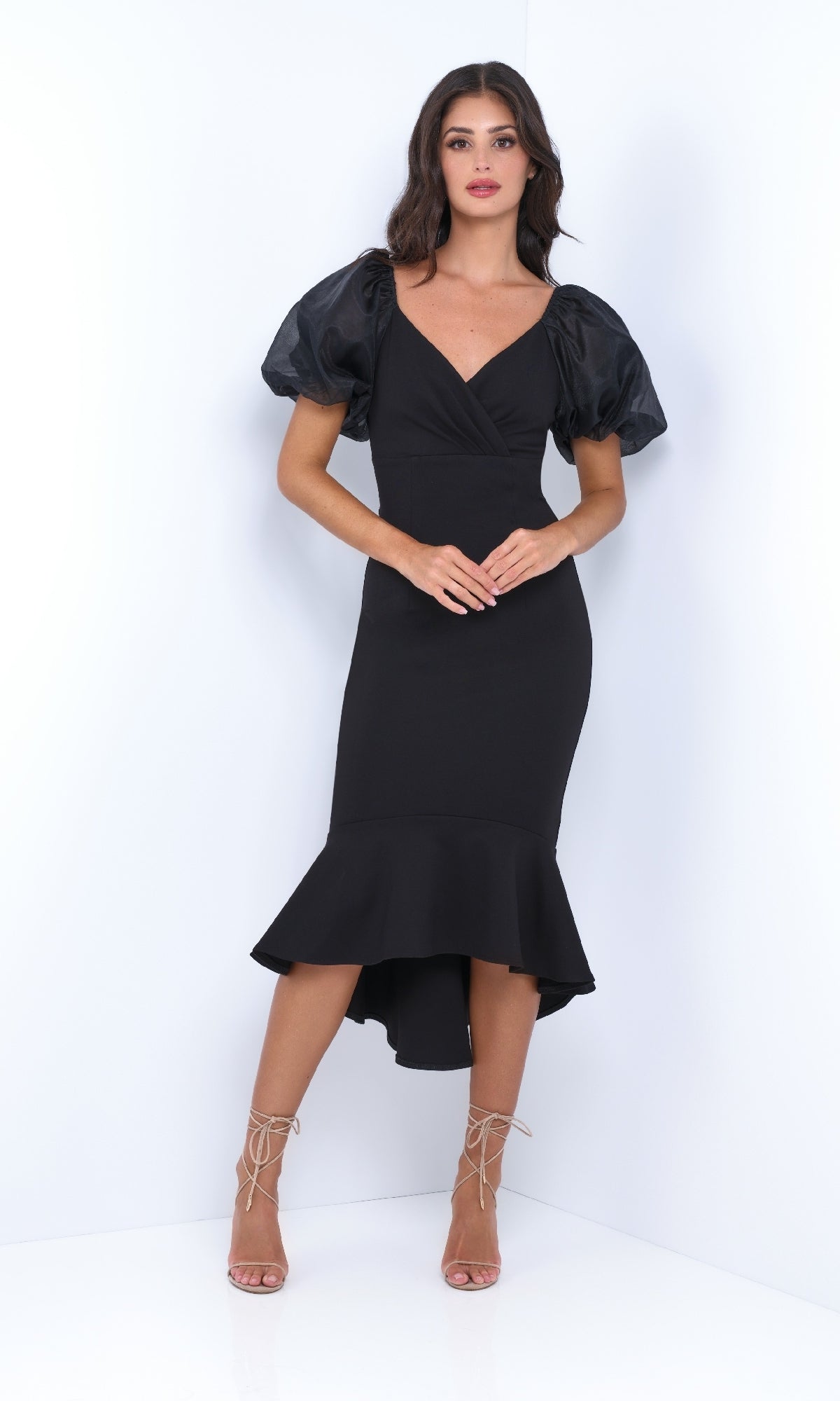 A woman stands against a white background wearing the Velvi Short Sleeve Midi Semi-Formal Dress Diana, featuring chic puffed sleeves and a ruffled high-low hem—an ideal stylish choice for any rehearsal dinner dress code.