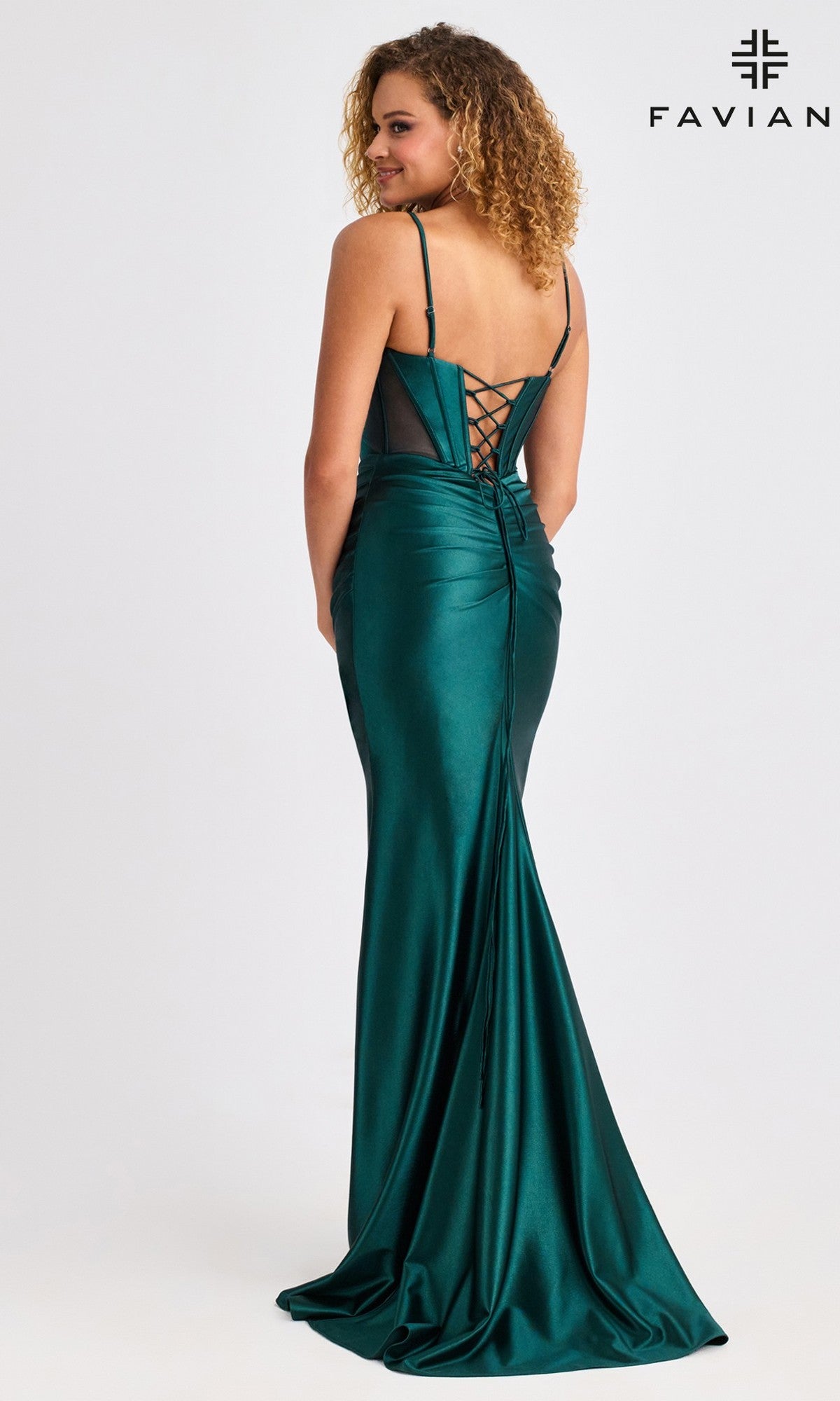 A woman faces away from the camera in the Faviana E11456 long prom dress—an emerald green satin gown featuring a lace-up back and corset bodice, set against a plain background.