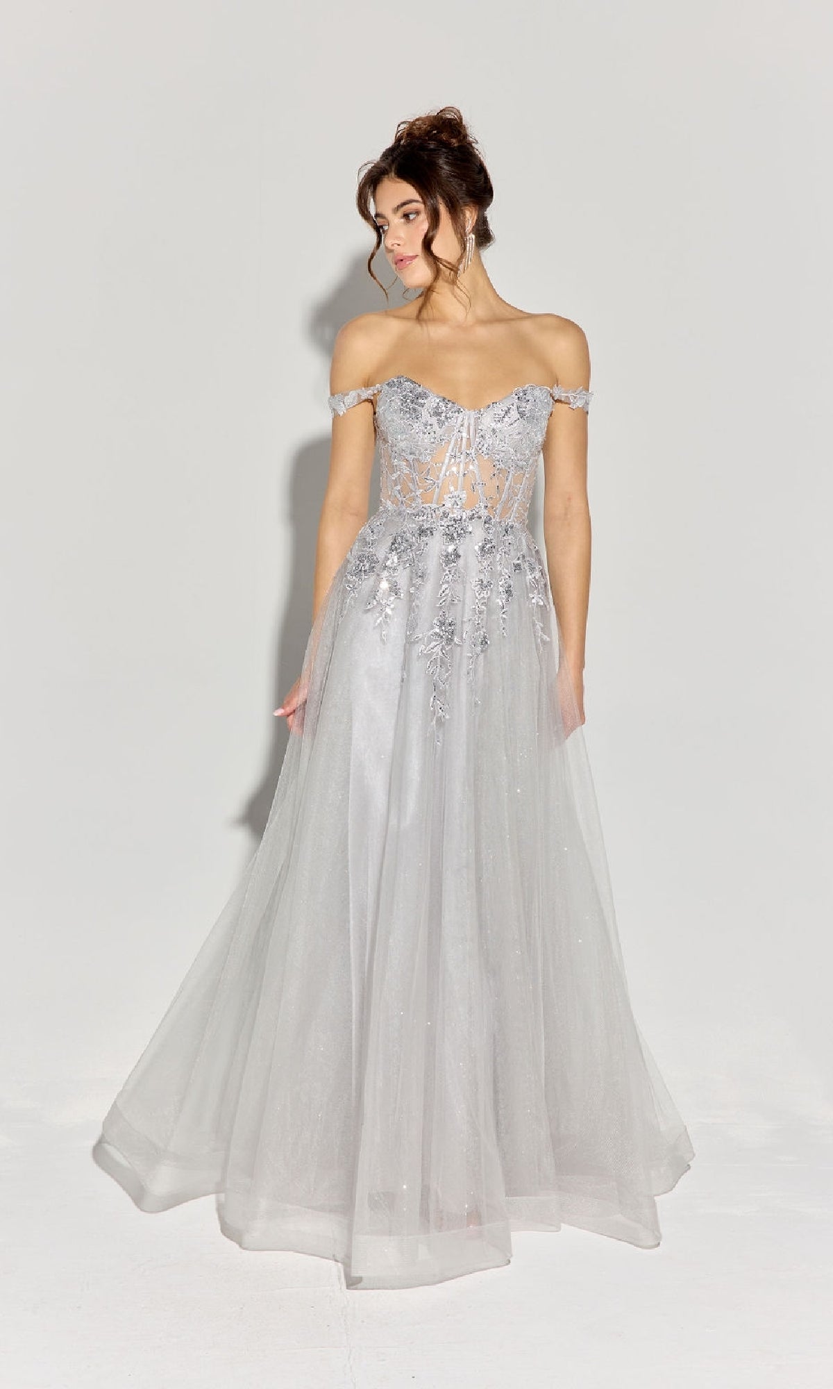 A woman wears the Off-Shoulder Long Prom Ball Gown: Eureka EK128, a light gray dress with a corset-style bodice and sheer floral details, standing against a plain white background.
