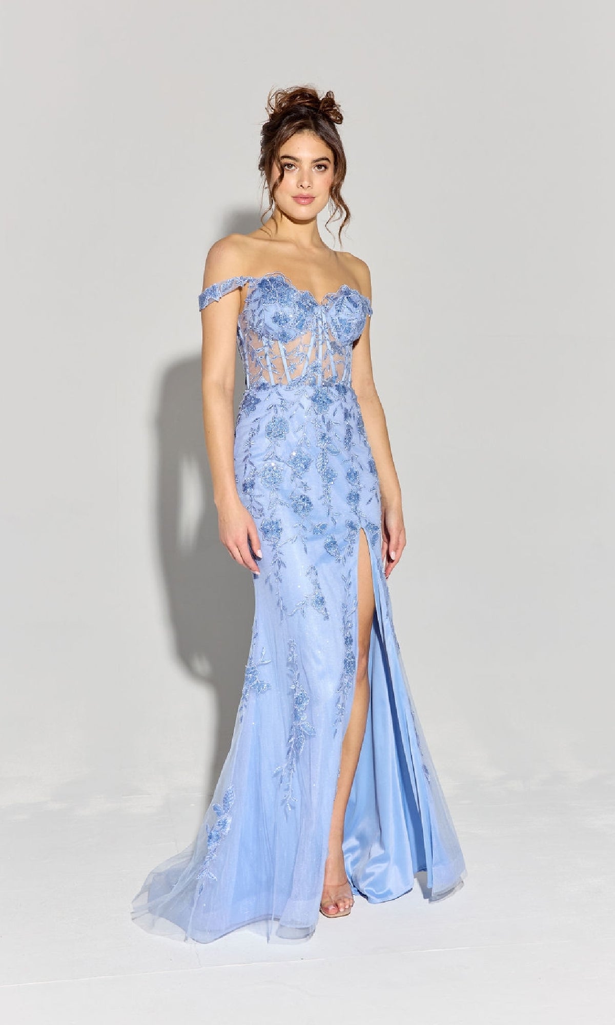 A woman stands against a plain background wearing the Eureka EK181, an off-shoulder long lace prom dress in light blue, featuring floral-lace embroidery and a thigh-high slit.