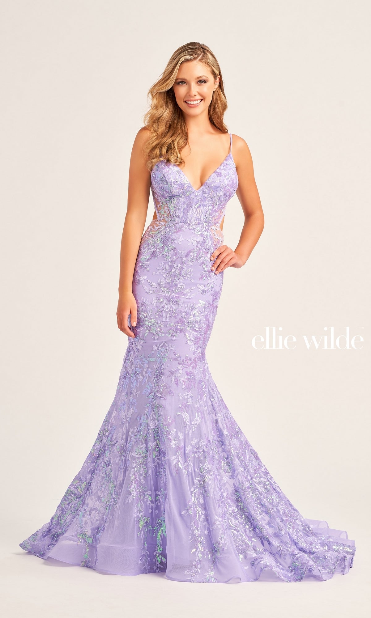 A woman wears the Ellie Wilde Long Tulle Designer Prom Dress EW35011—a fitted lavender sequin floral gown with thin straps and a mermaid silhouette—standing against a plain light background.