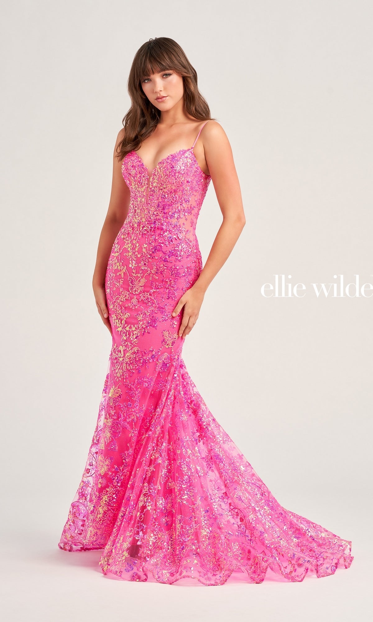 A woman wears the Ellie Wilde Designer Glitter Prom Dress EW35013—a floor-length, pink sequin mermaid gown with thin straps and a fitted, flared silhouette—posed against a plain light background.