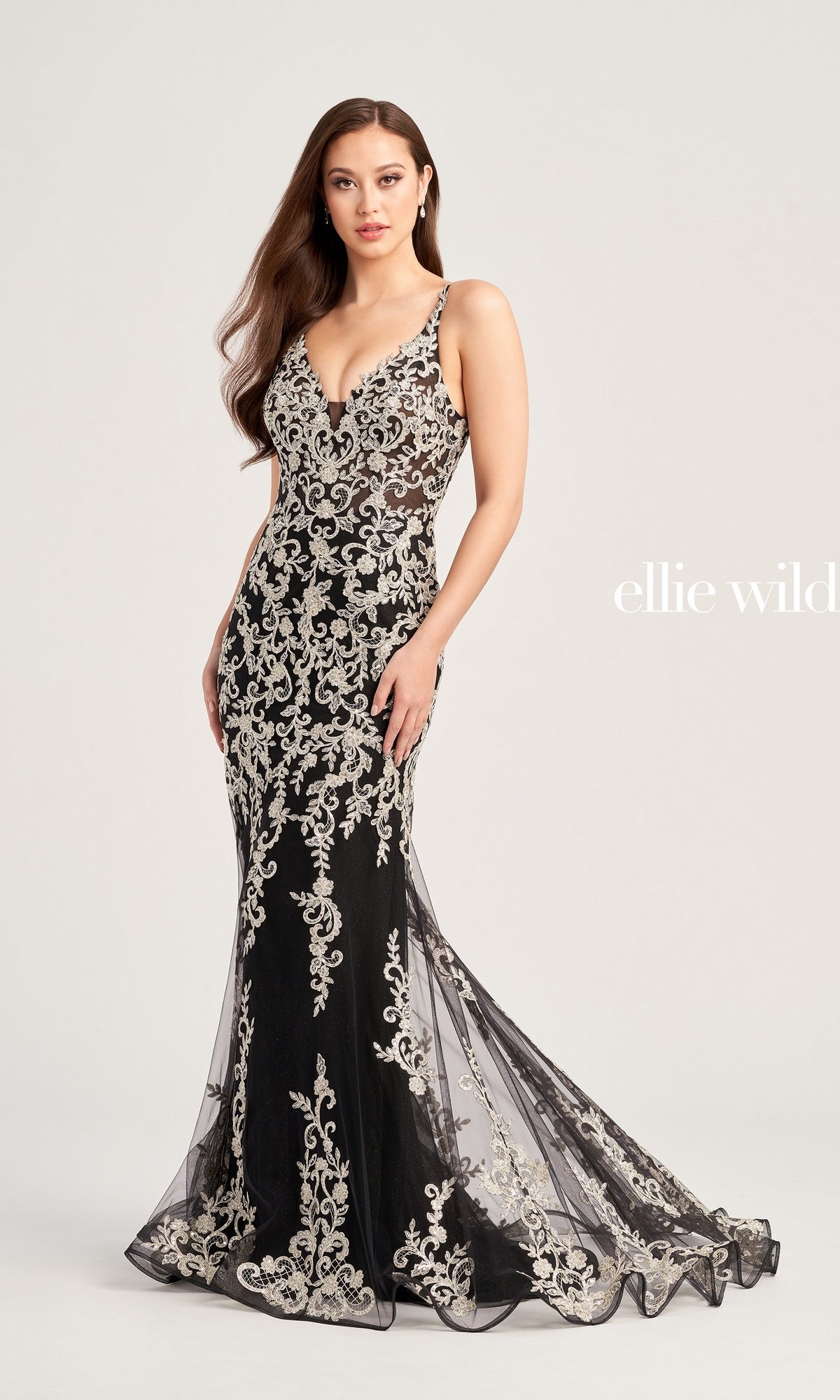 A woman models the Ellie Wilde Long Glitter-Lace Prom Dress EW35071—an elegant fitted black gown with silver floral embroidery—against a plain light background.