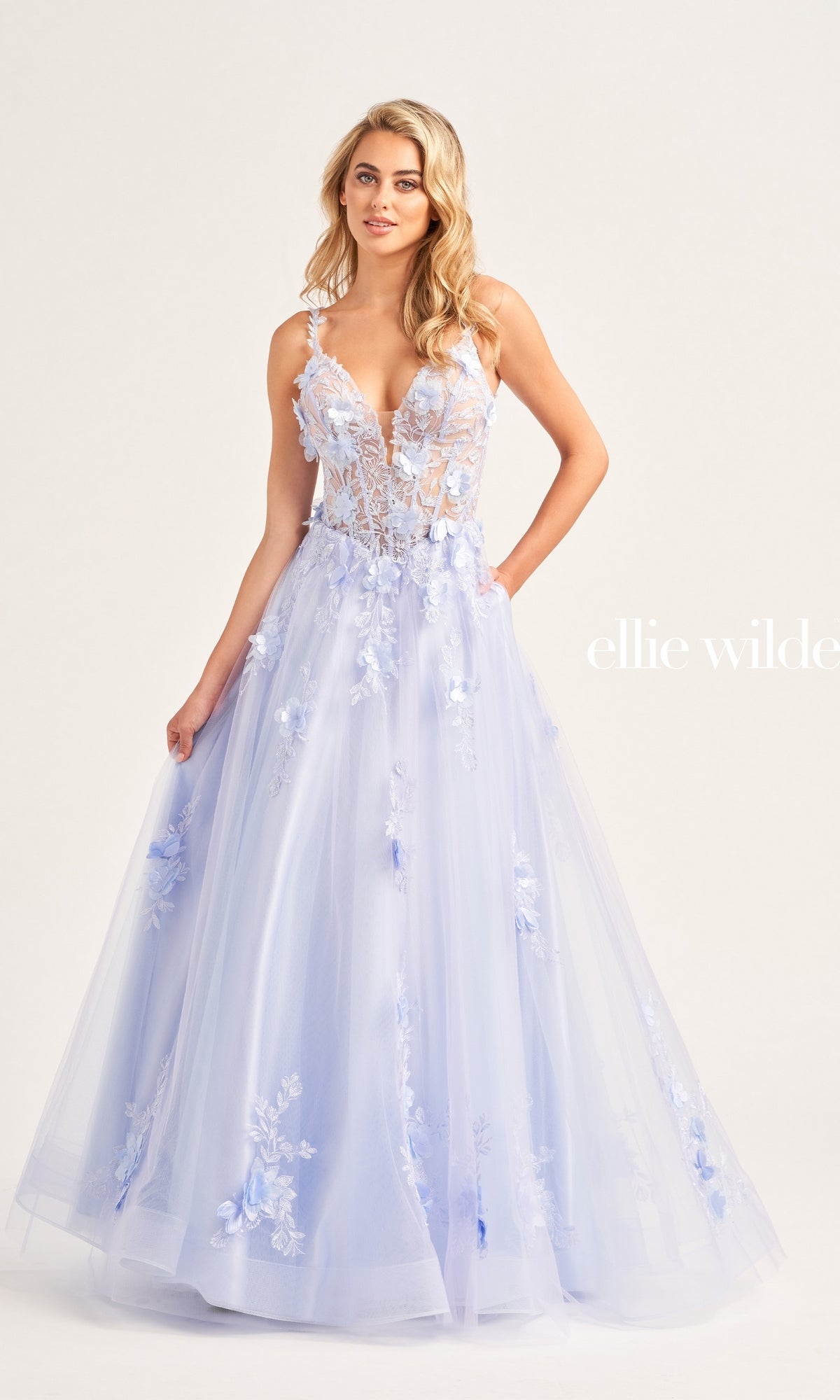 A woman wearing an Ellie Wilde Bright Pink Prom Ball Gown EW35122 with a sheer, corset-style bodice and spaghetti straps stands against a plain background.