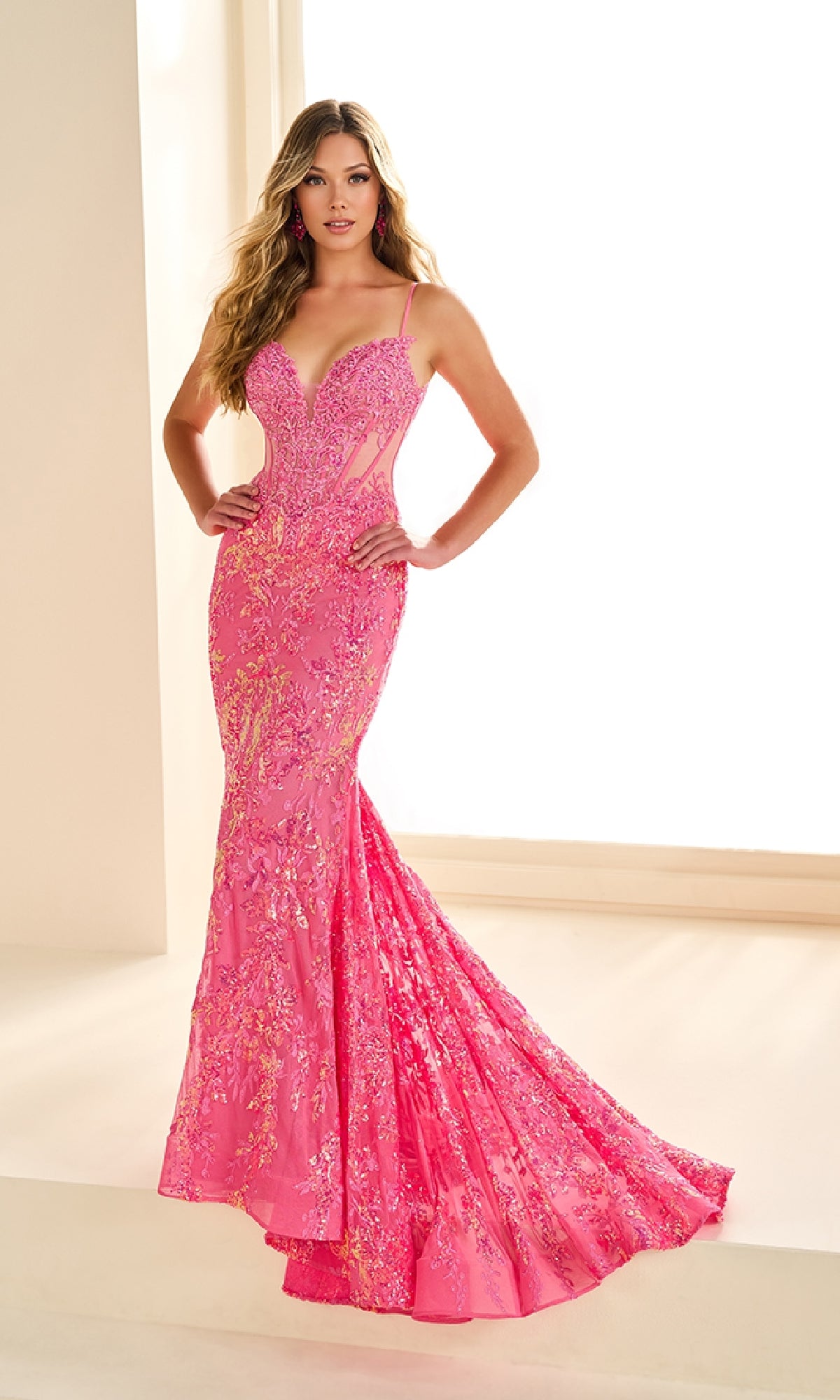 A woman stands indoors wearing the Ellie Wilde EW36003 Sequin-Print Mermaid Prom Dress, featuring a fitted floor-length silhouette, sheer corset bodice, and flared train.