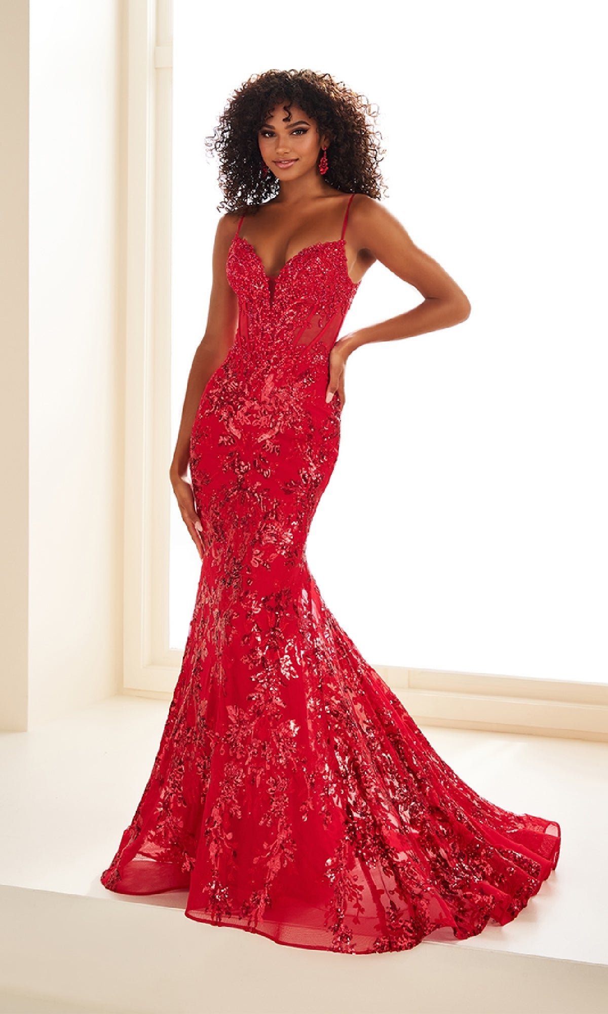 A woman poses with one hand on her hip in front of a bright white background, wearing the Ellie Wilde EW36003: a fitted, floor-length sequin-print mermaid prom dress with thin straps.