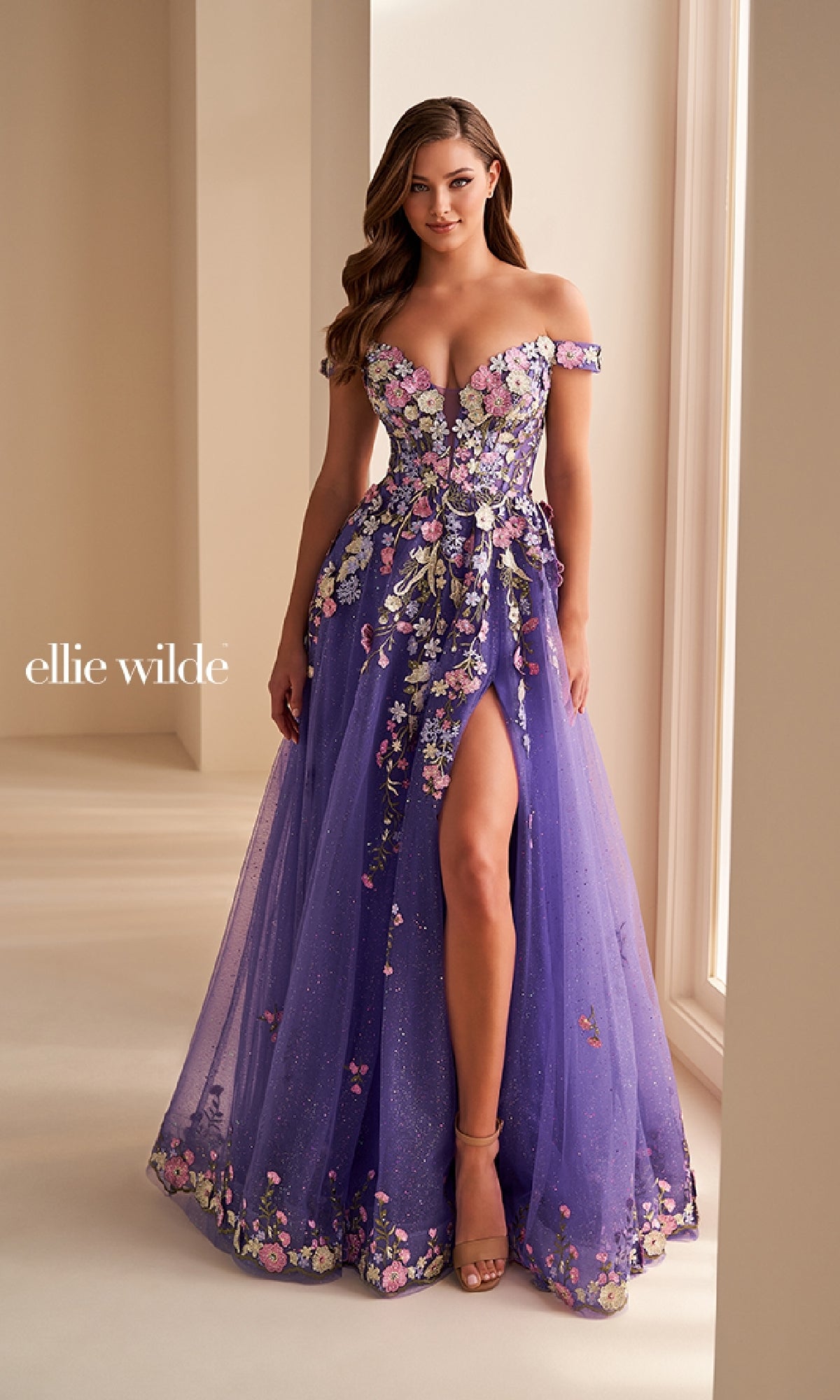 Woman wearing the Ellie Wilde EW36215 long prom dress in purple with floral embroidery, a thigh-high slit, and sheer skirt indoors.