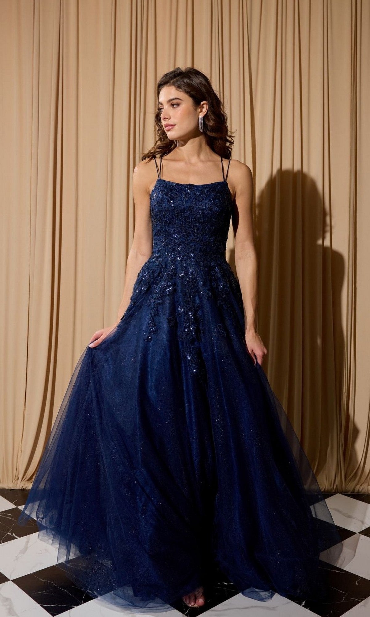 A woman in the Eureka EK197 long prom dress in navy stands on a black and white checkered floor before beige curtains.