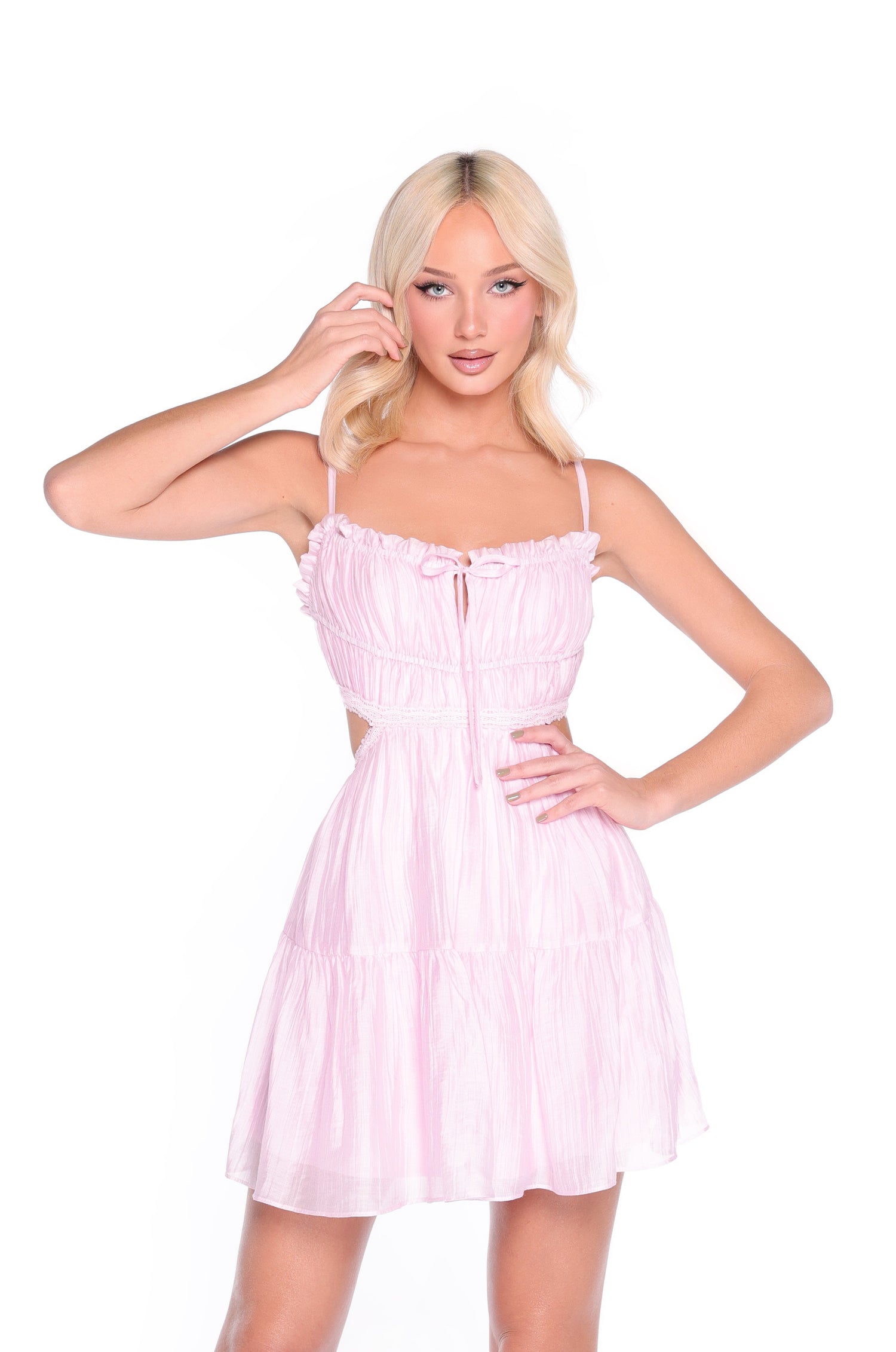 A woman with long blonde hair models the Pink Open-Back Casual Summer Dress: Elara, featuring ruffle details, an a-line skirt, and cutout sides, as she poses against a plain white background.