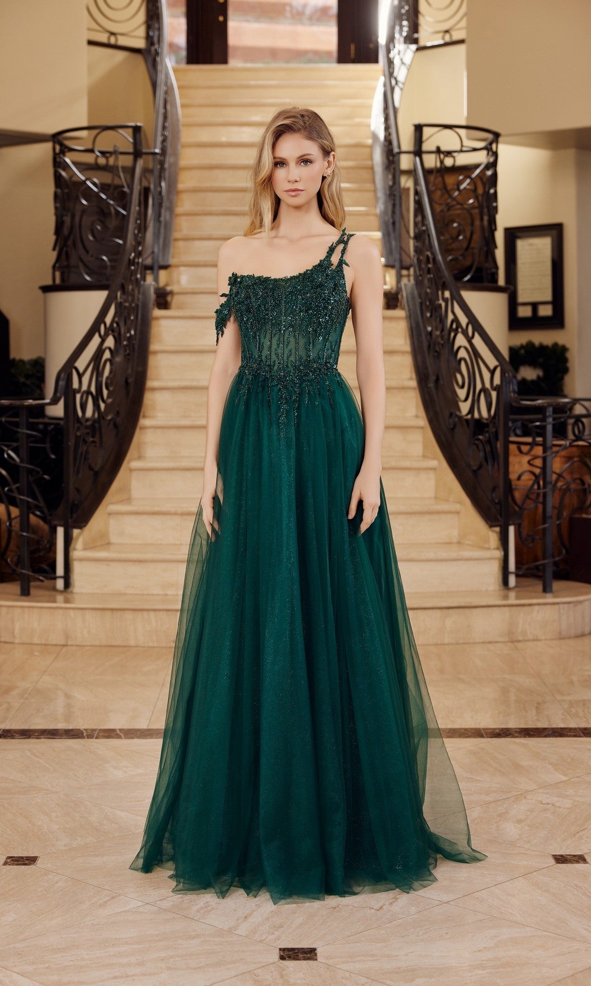 A woman in the Nox Anabel F1567 Asymmetrical Glitter Prom Dress poses before a grand staircase with ornate railings in an elegant interior setting.
