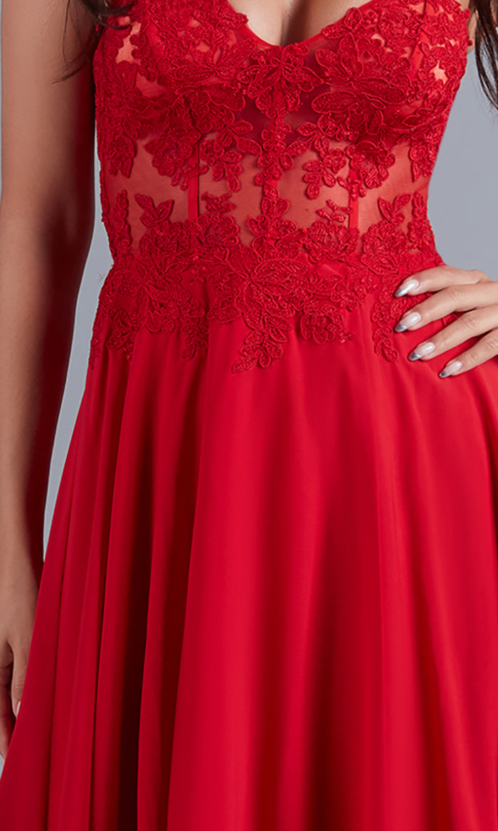 A woman poses confidently with one hand on her hip, wearing the Long Red Sheer-Bodice Prom Dress by PromGirl, featuring a lace sleeveless bodice and a flowing skirt.