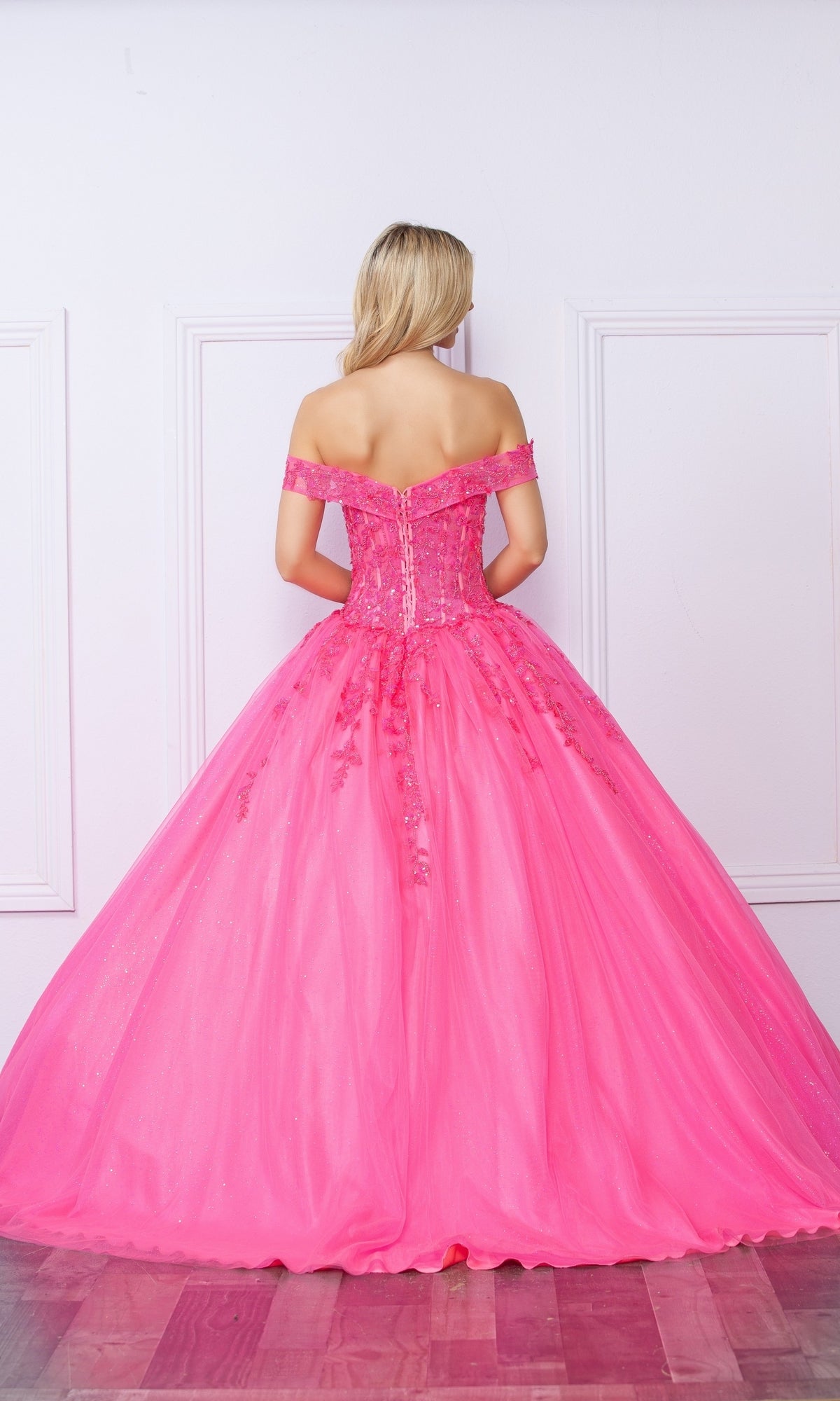A blonde woman faces away, wearing the Bright Off-the-Shoulder Long Prom Ball Gown H1349—a floor-length, vibrant pink dress with a full skirt and lace details.