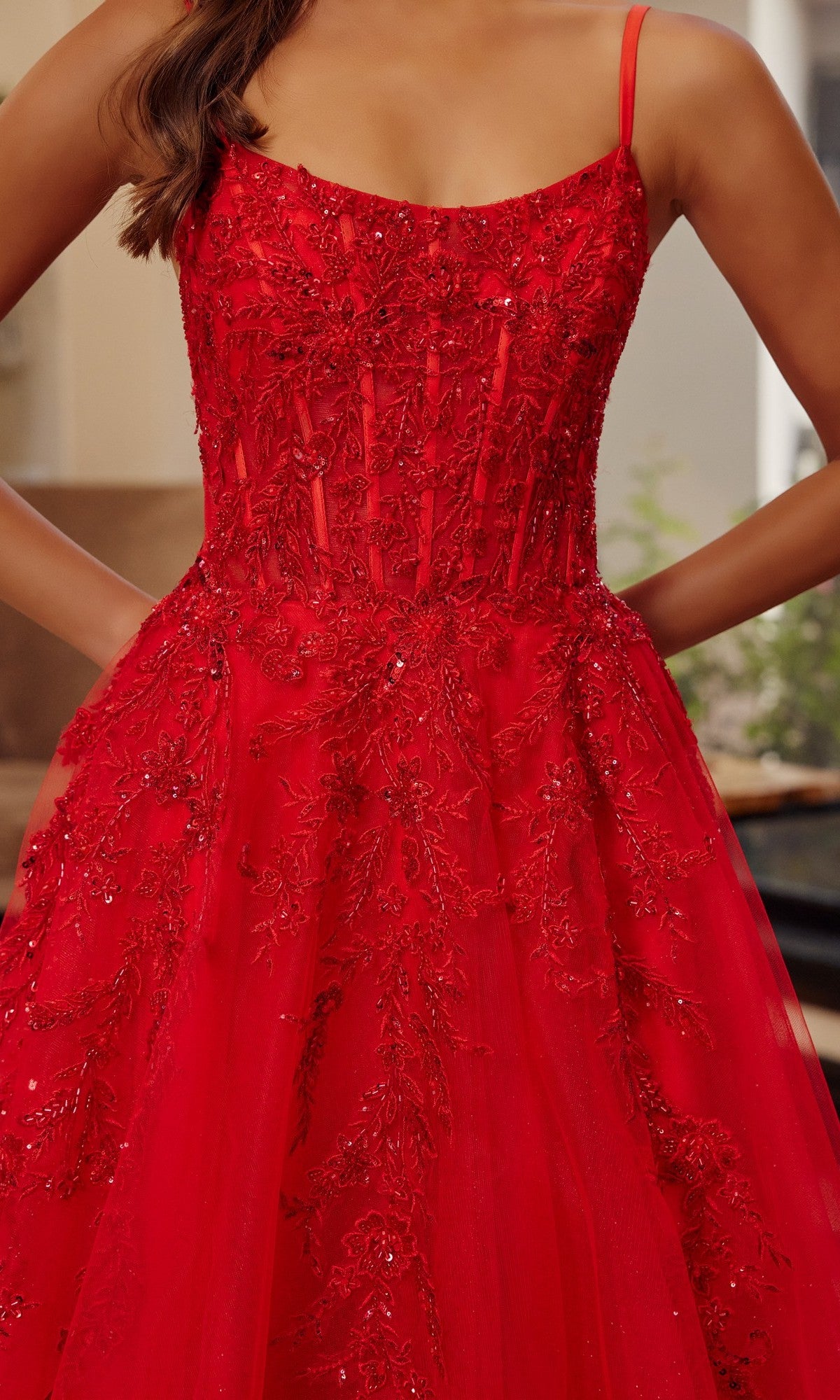 A woman stands confidently with hands on hips, wearing the Nox Anabel H1886 long prom dress—sleeveless, with a fitted red bodice adorned in intricate beadwork and floral embroidery, and a flowing tulle A-line skirt.