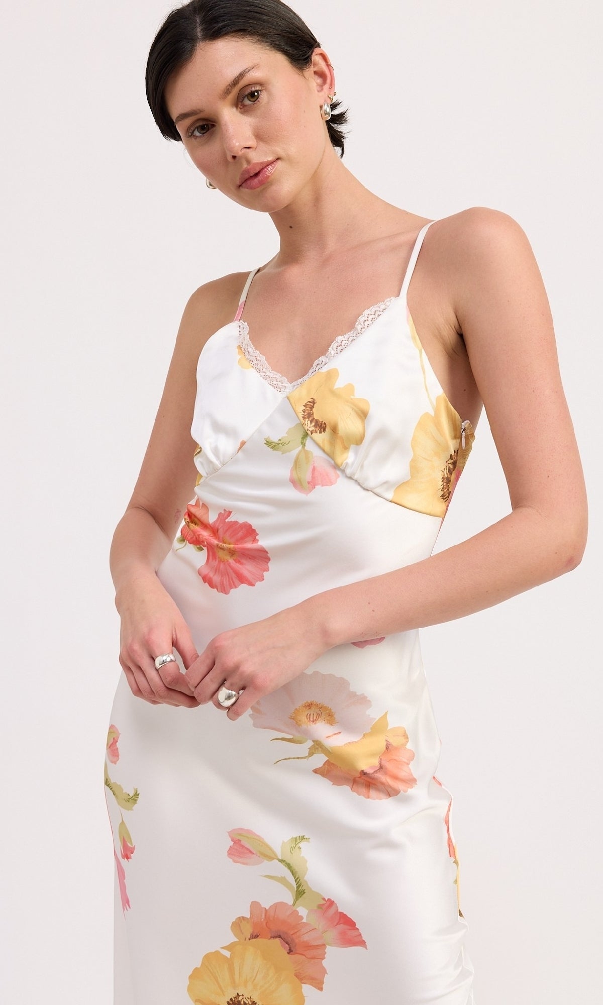 A woman models the V-Neck Floral Print Midi Slip Dress, featuring thin straps, a sheath silhouette, and yellow and pink flowers against a plain background.