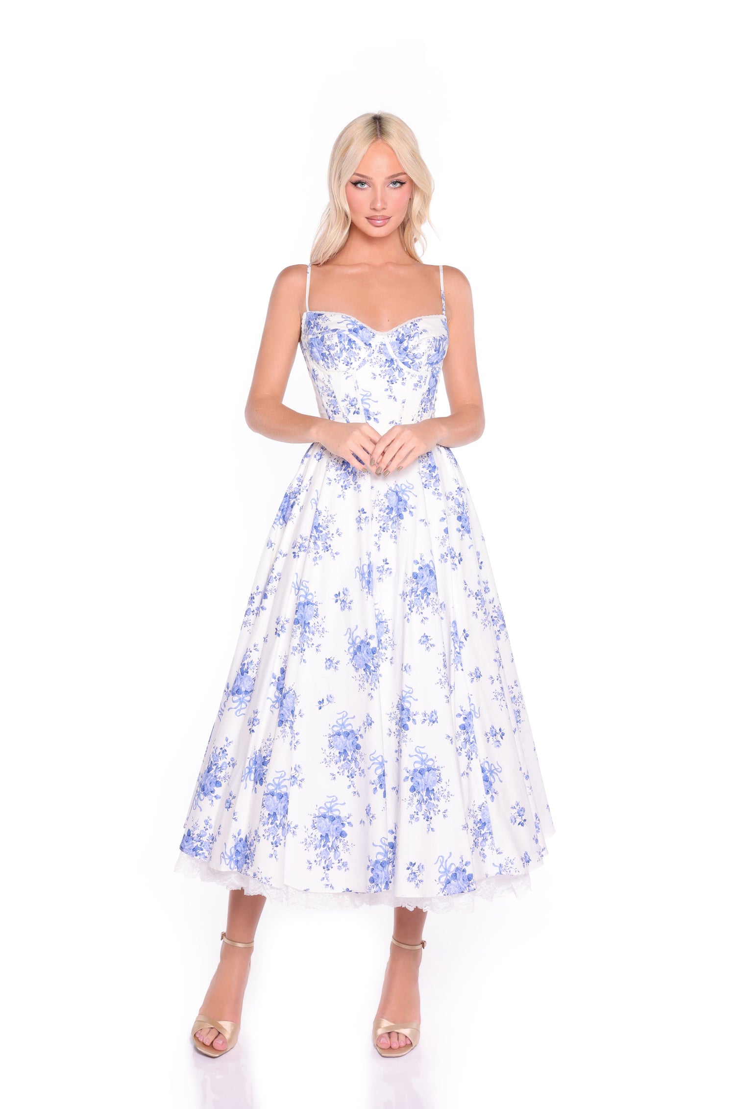 Woman wearing the Isolde White & Blue Floral Midi Summer Dress, featuring a corset bodice and thin straps, styled with nude heels against a white background.