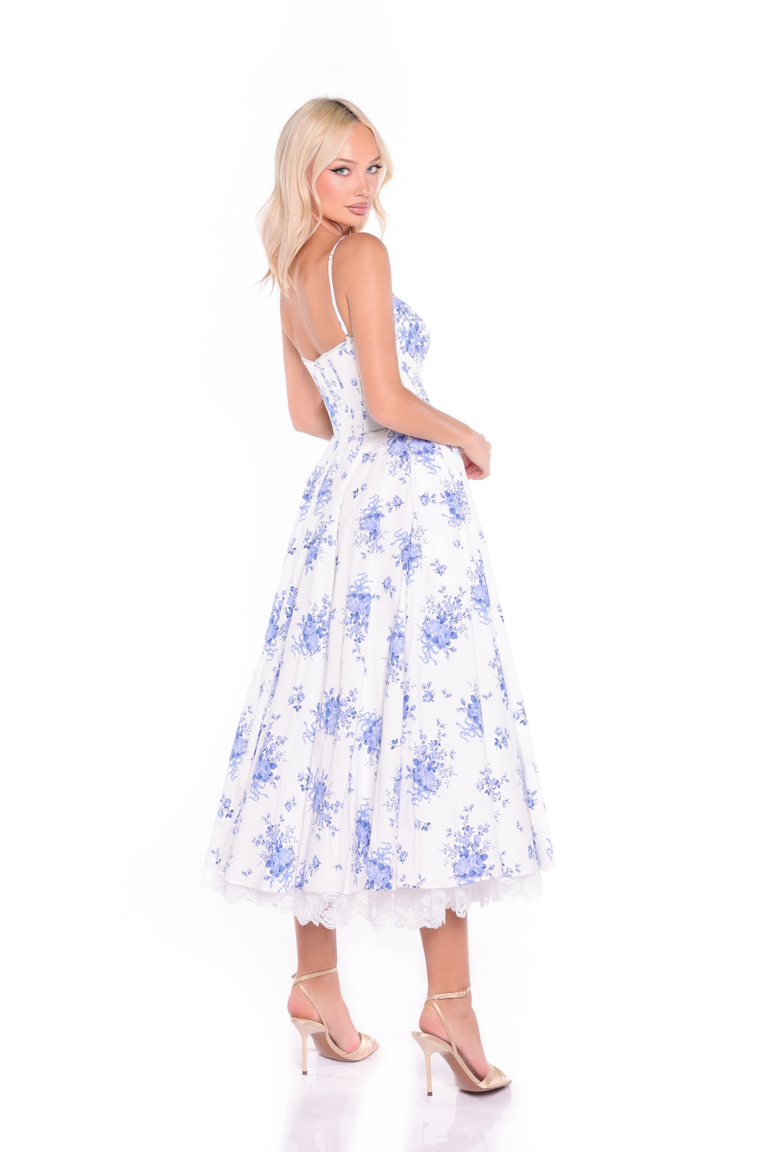 Woman facing backward, looking over her shoulder, wearing the Isolde White & Blue Floral Midi Summer Dress with corset bodice and beige heels against a white background.