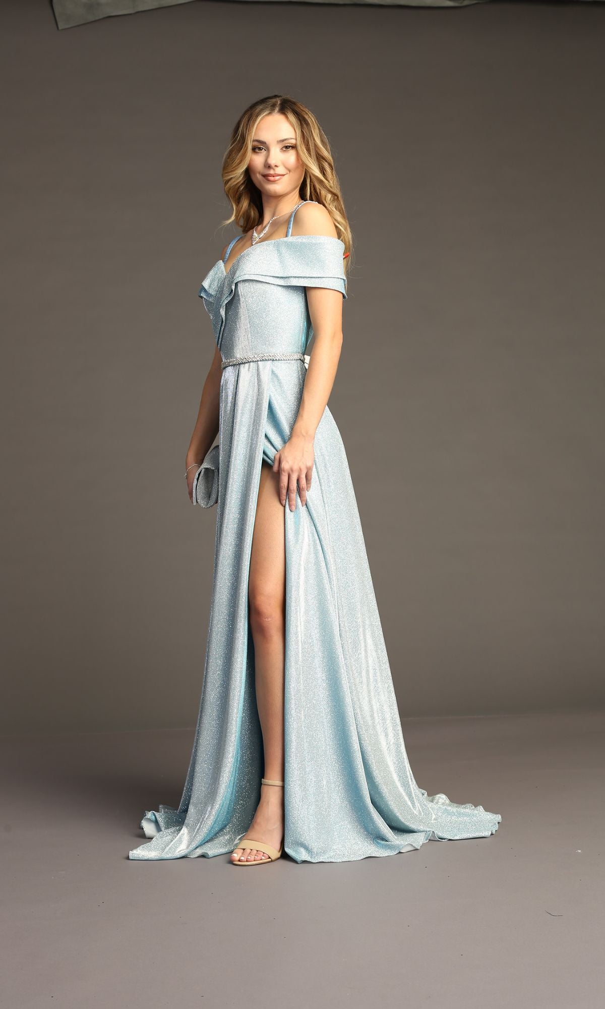 Woman in the Off-Shoulder Long Glitter Prom Dress: Chicas J008, featuring a high slit, holding a clutch against a plain background.