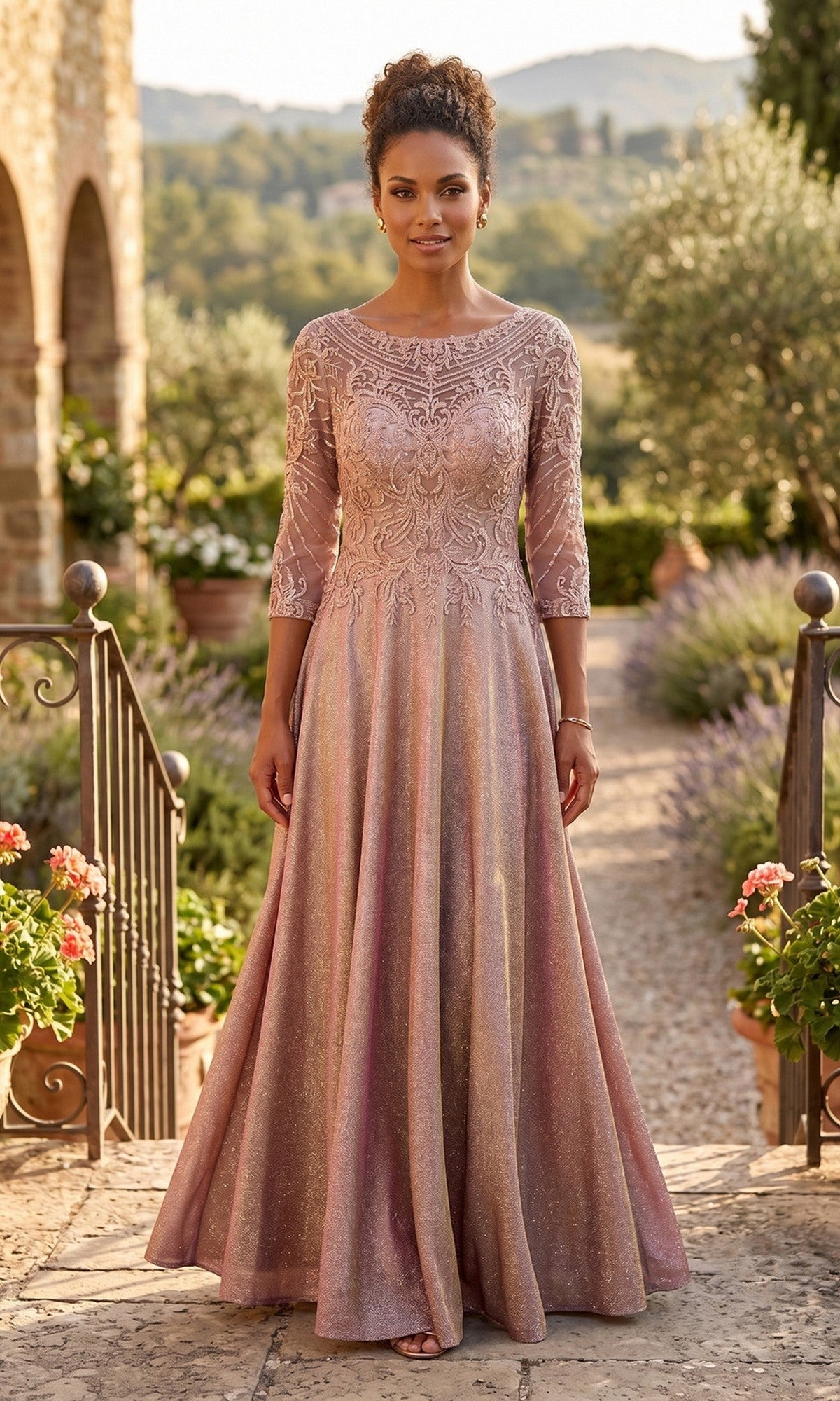 A woman wears the Long Formal Dress: Chicas J052 in shimmering rose gold with three-quarter sleeves, standing outdoors on a stone path among greenery and distant hills.