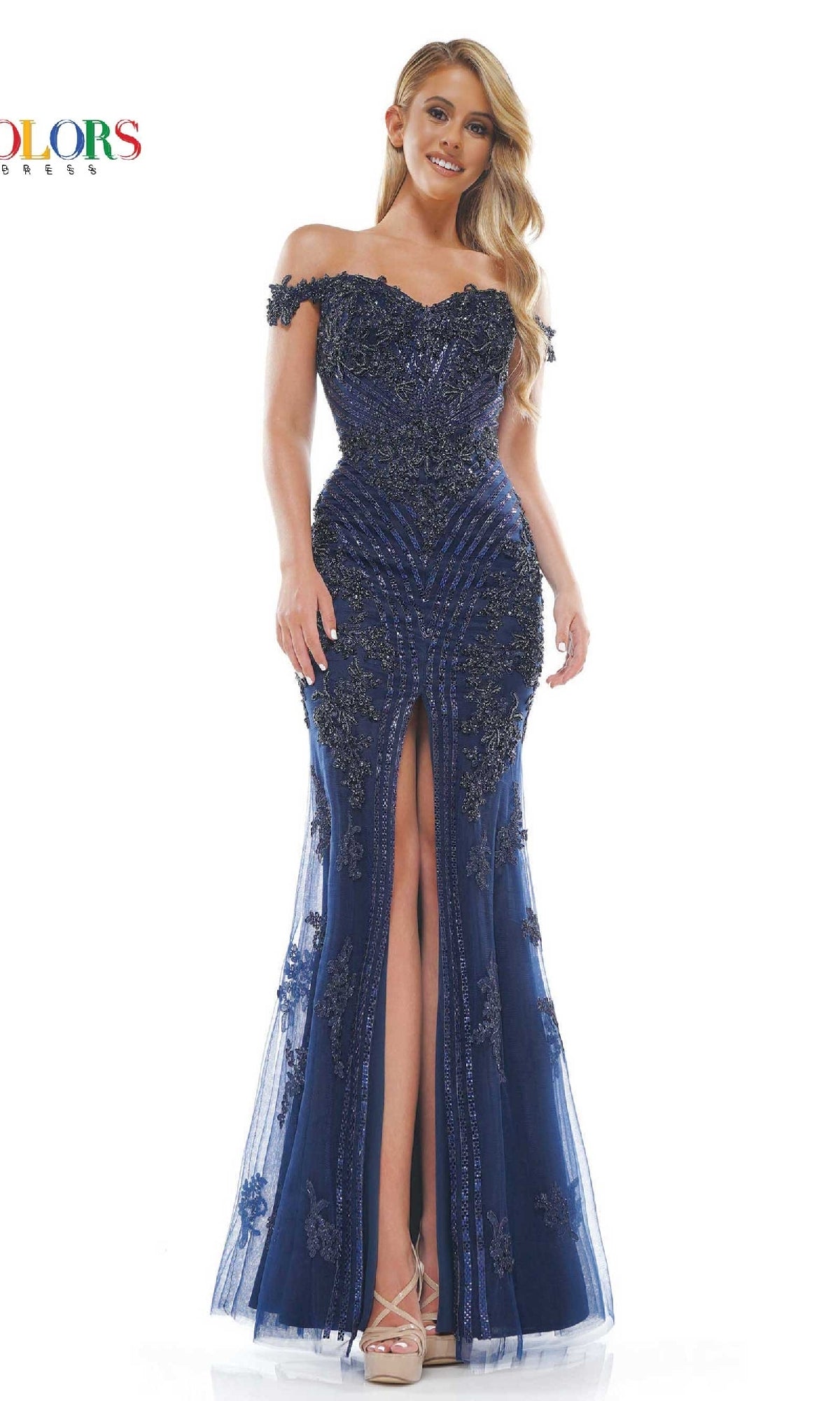 A woman models the Colors Dress J131, an off-shoulder beaded prom dress in navy blue with embellishments and a front slit, against a white background.