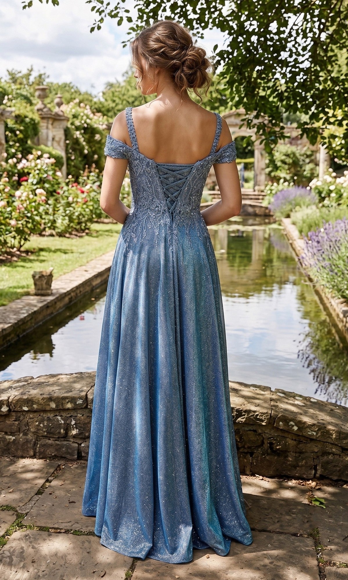 A woman wearing the Long Prom Dress: Chicas J169, a sparkly blue off-shoulder gown with an embellished bodice, stands on a stone path beside a reflective pond in a garden, facing away from the camera.