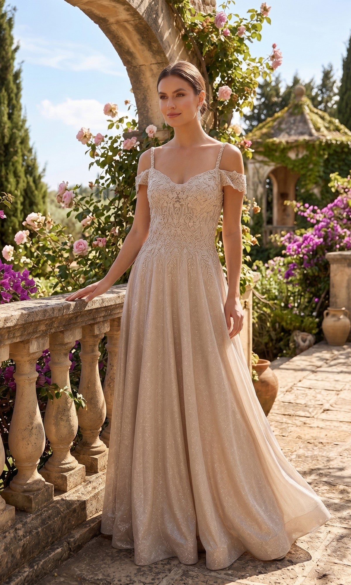 A woman in a champagne Long Prom Dress: Chicas J169 with an off-shoulder lace design and embellished bodice stands on a stone terrace surrounded by blooming flowers and greenery on a sunny day.