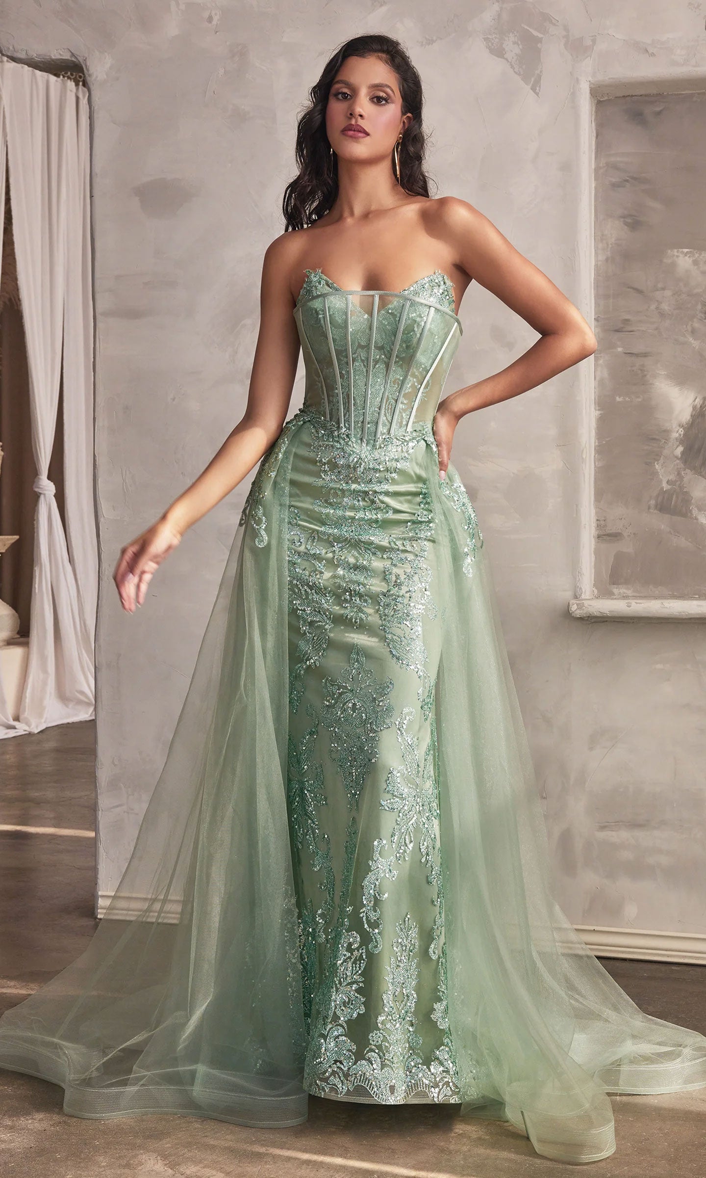A woman stands indoors against a neutral background wearing the Glitter-Print Strapless Long Prom Dress J858, a light green mermaid gown with sheer panels, lace detailing, and a tulle overskirt.
